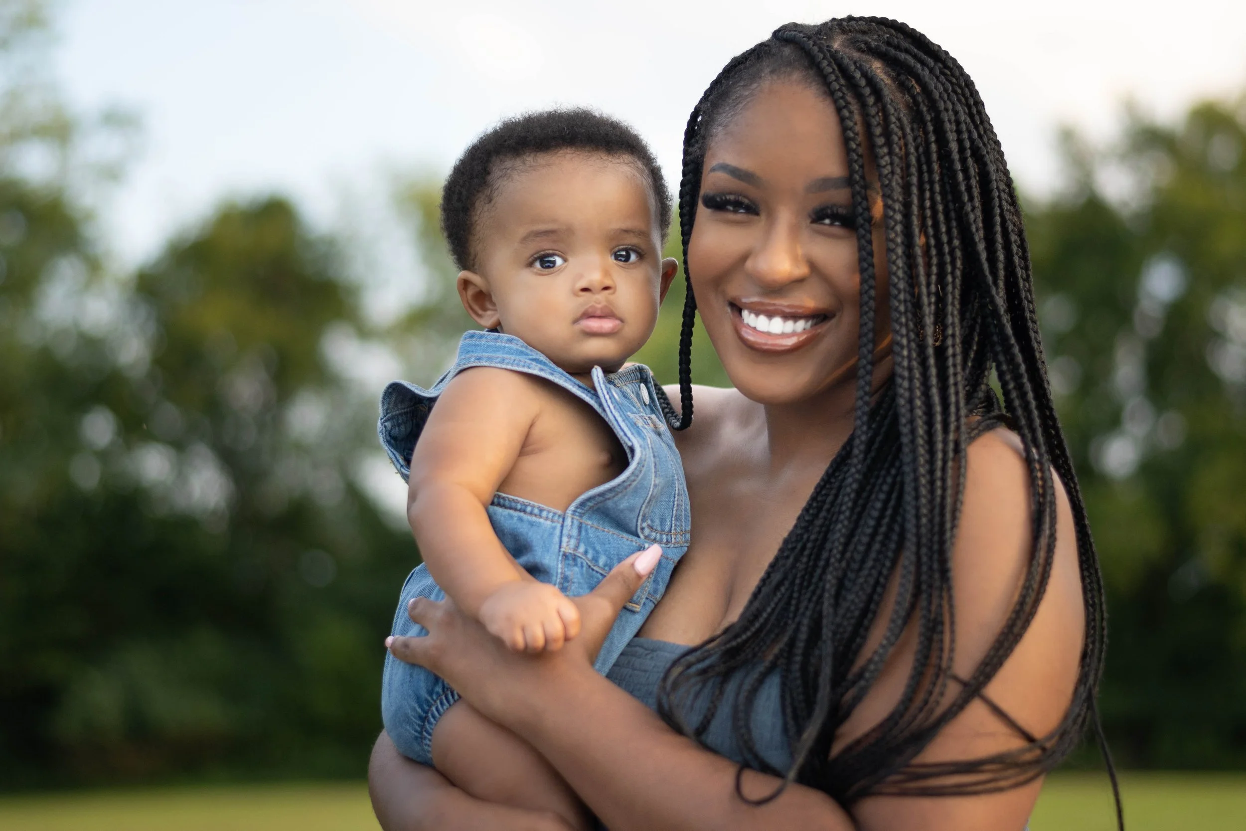 Yevette Lynn, lifestyle photographer, captures an outdoor portrait of a mother holding her baby, both smiling softly in natural daylight.