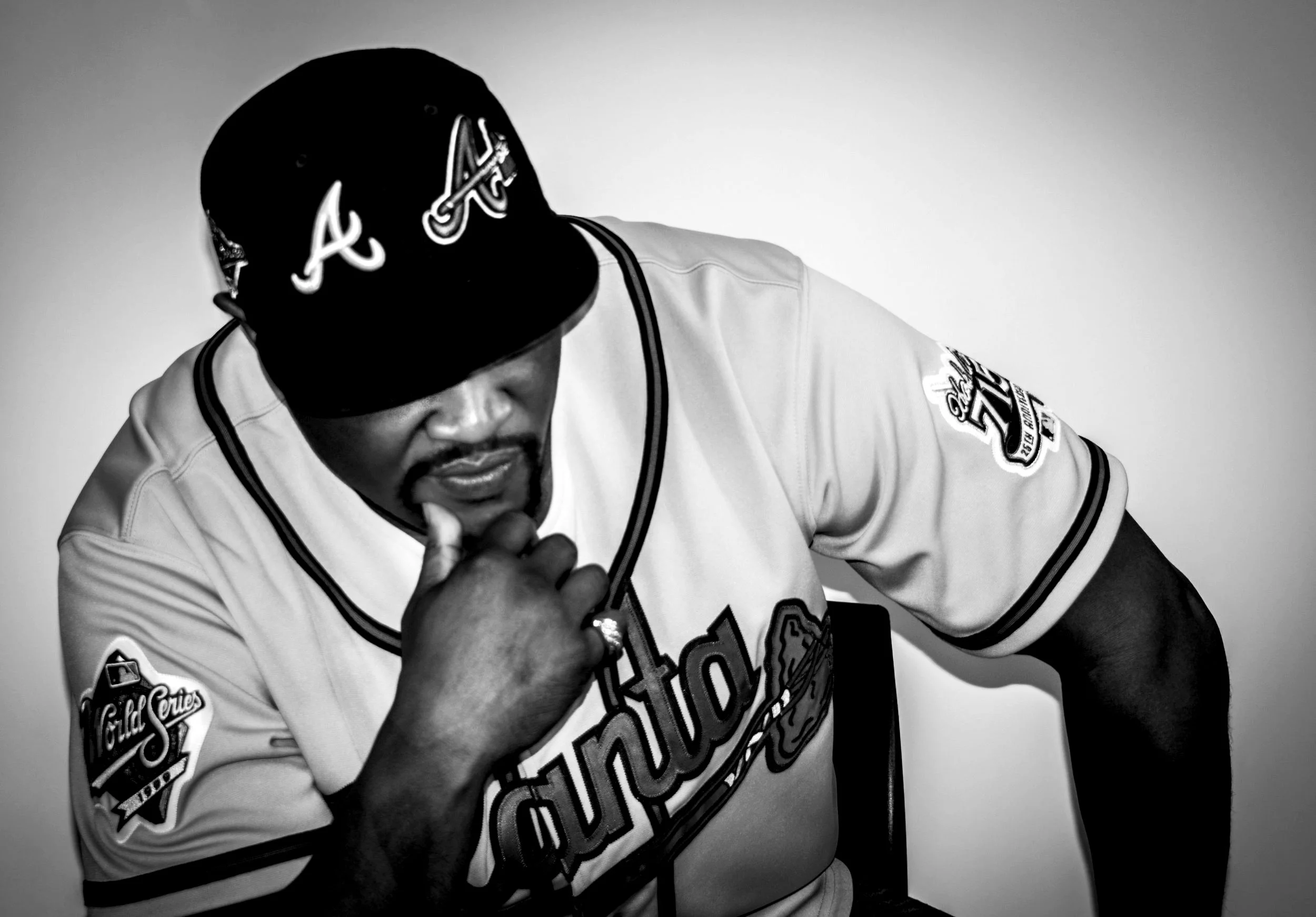 Yevette Lynn portrait photographer captures black and white studio portrait of man in baseball jersey and cap, posed thoughtfully with hand on chin.