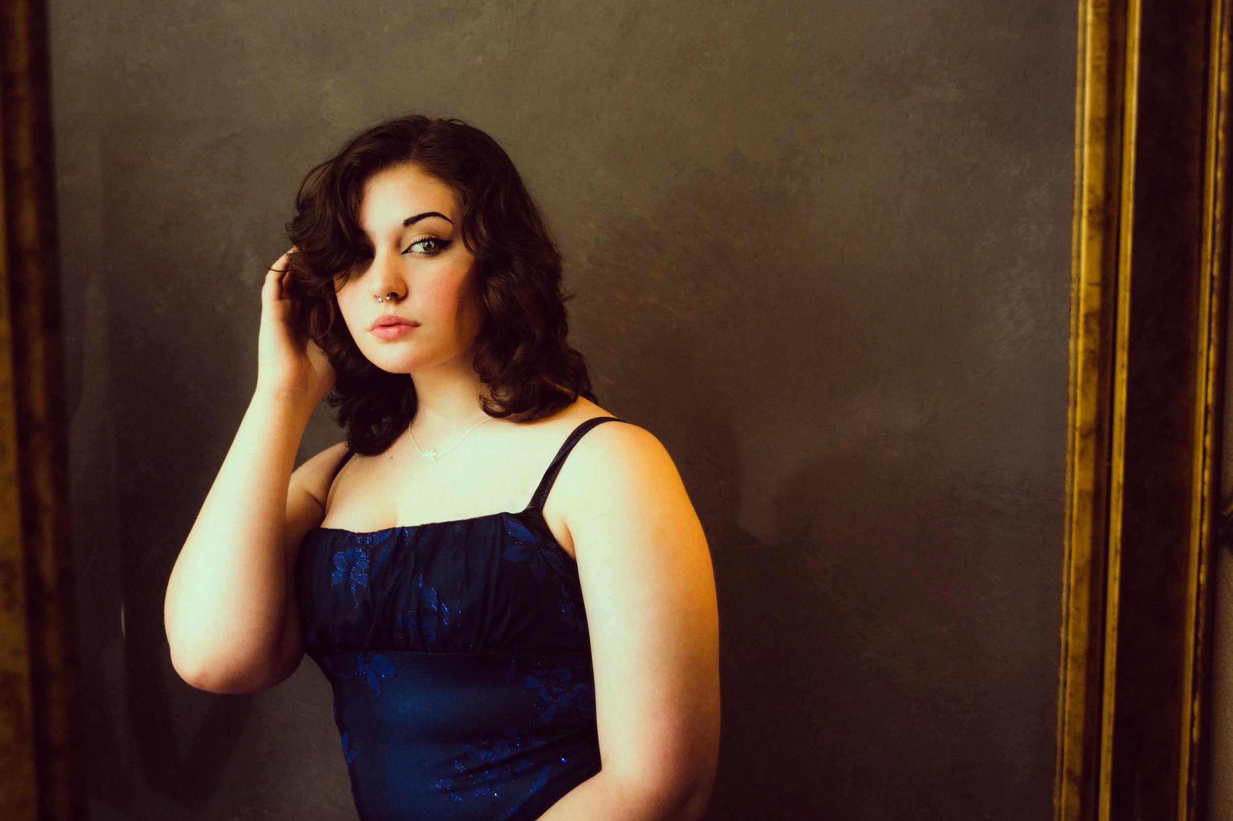 Yevette Lynn portrait photographer captures studio portrait of woman with dark wavy hair and nose ring, softly posed against textured, moody backdrop.
