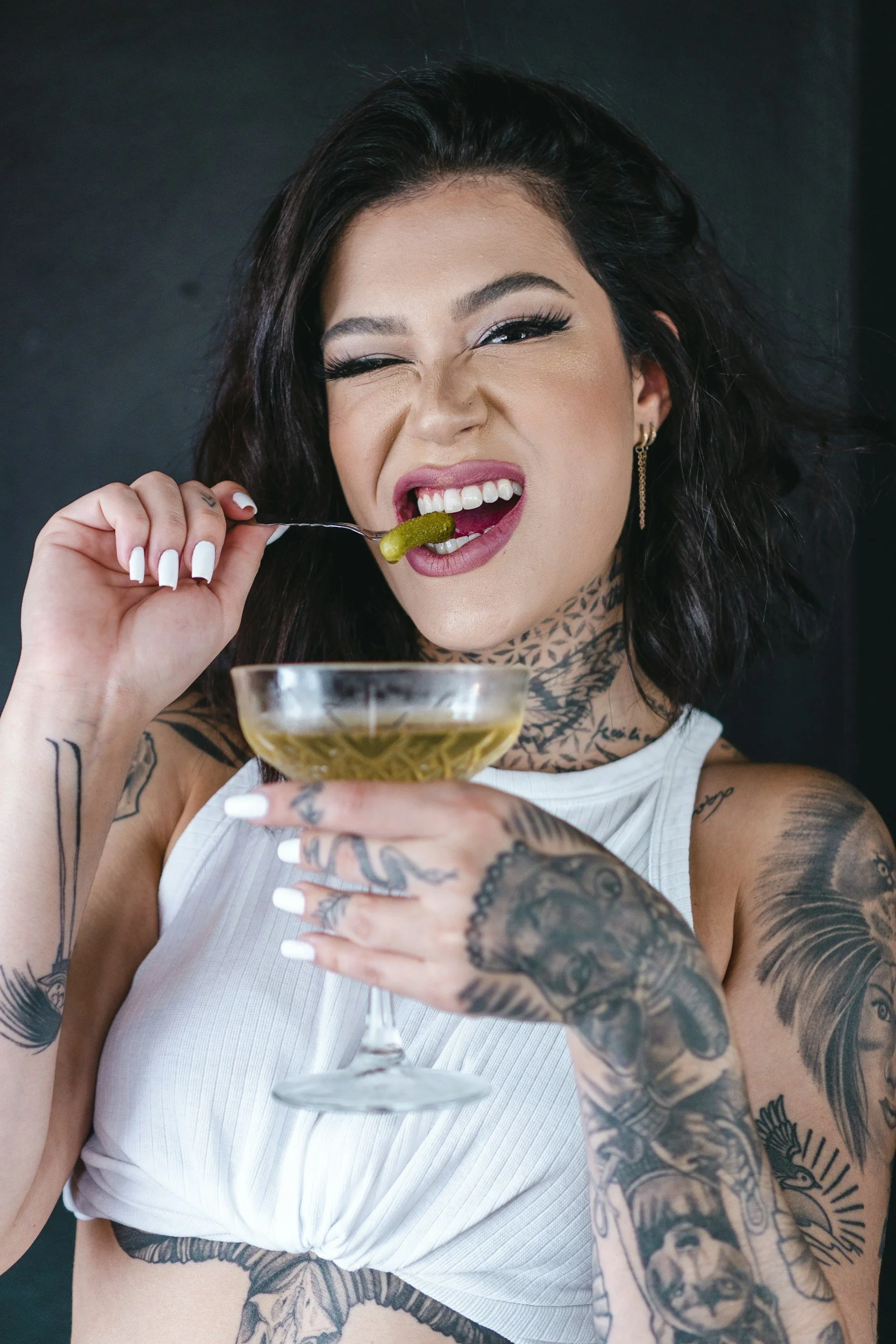 Tattooed woman holding cocktail and citrus garnish, intimate studio lifestyle portrait with bold, modern expression.