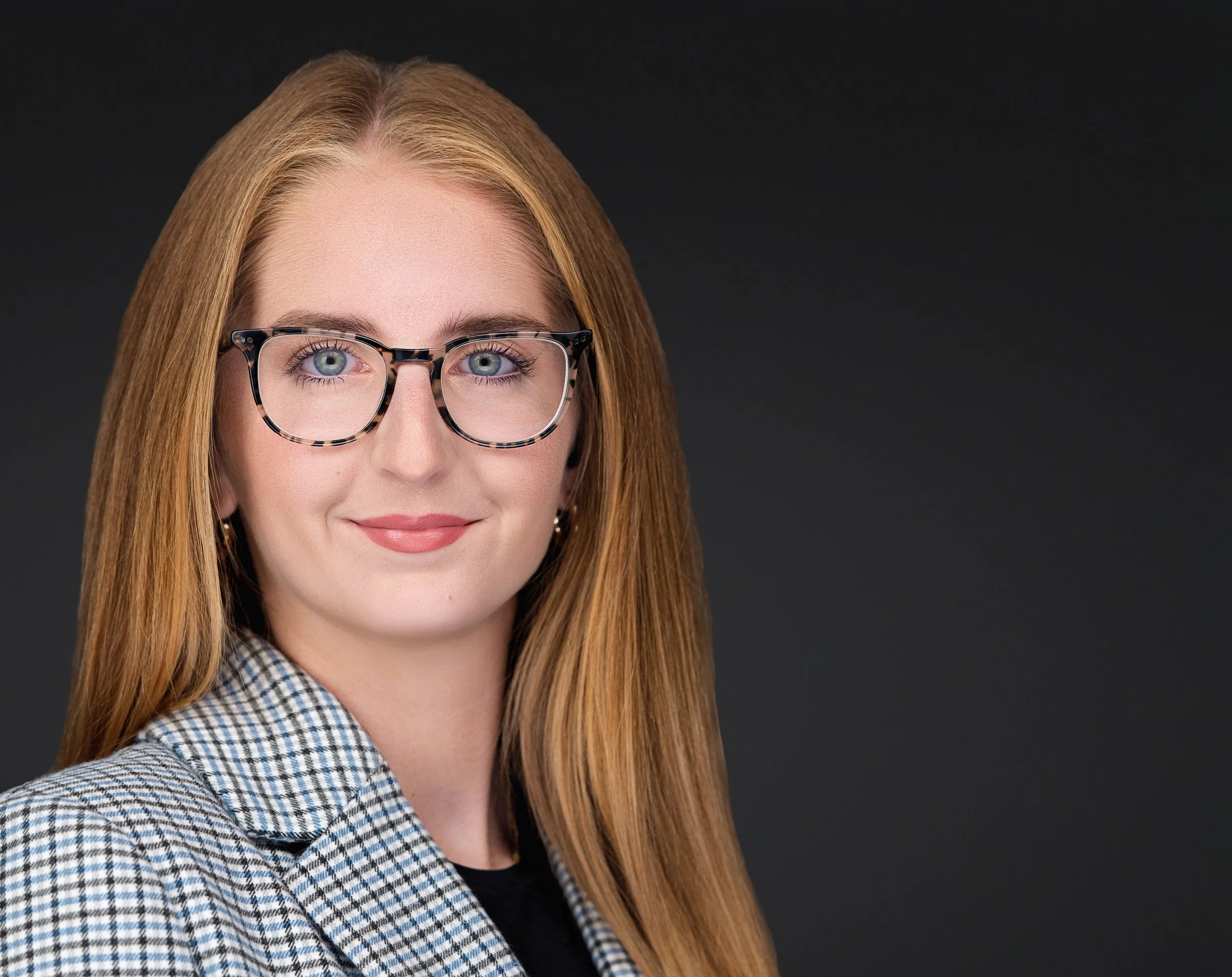 Yevette Lynn, professional photographer, creates a clean studio headshot for branding, featuring a woman with glasses against a dark neutral background.