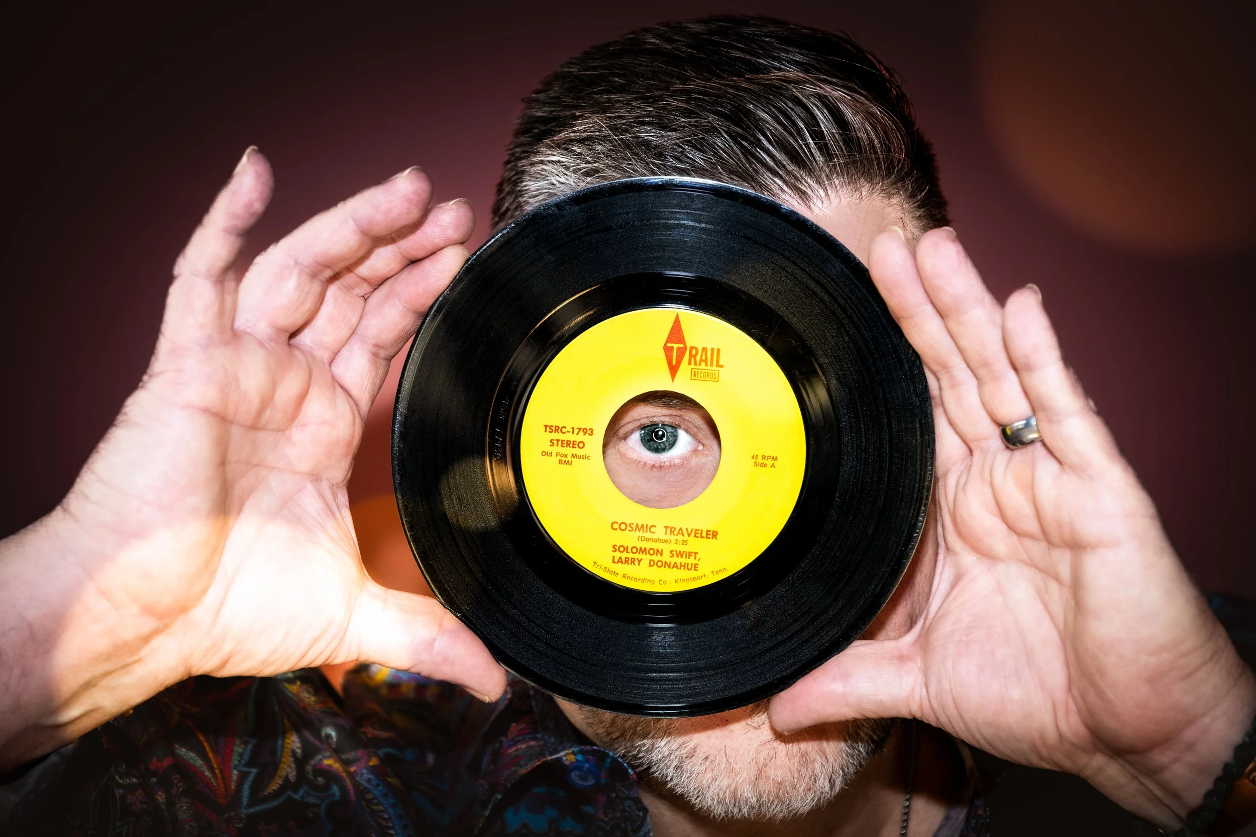 Yevette Lynn portrait photographer captures studio portrait of local vinyl record collector and radio personality holding vintage record over face.