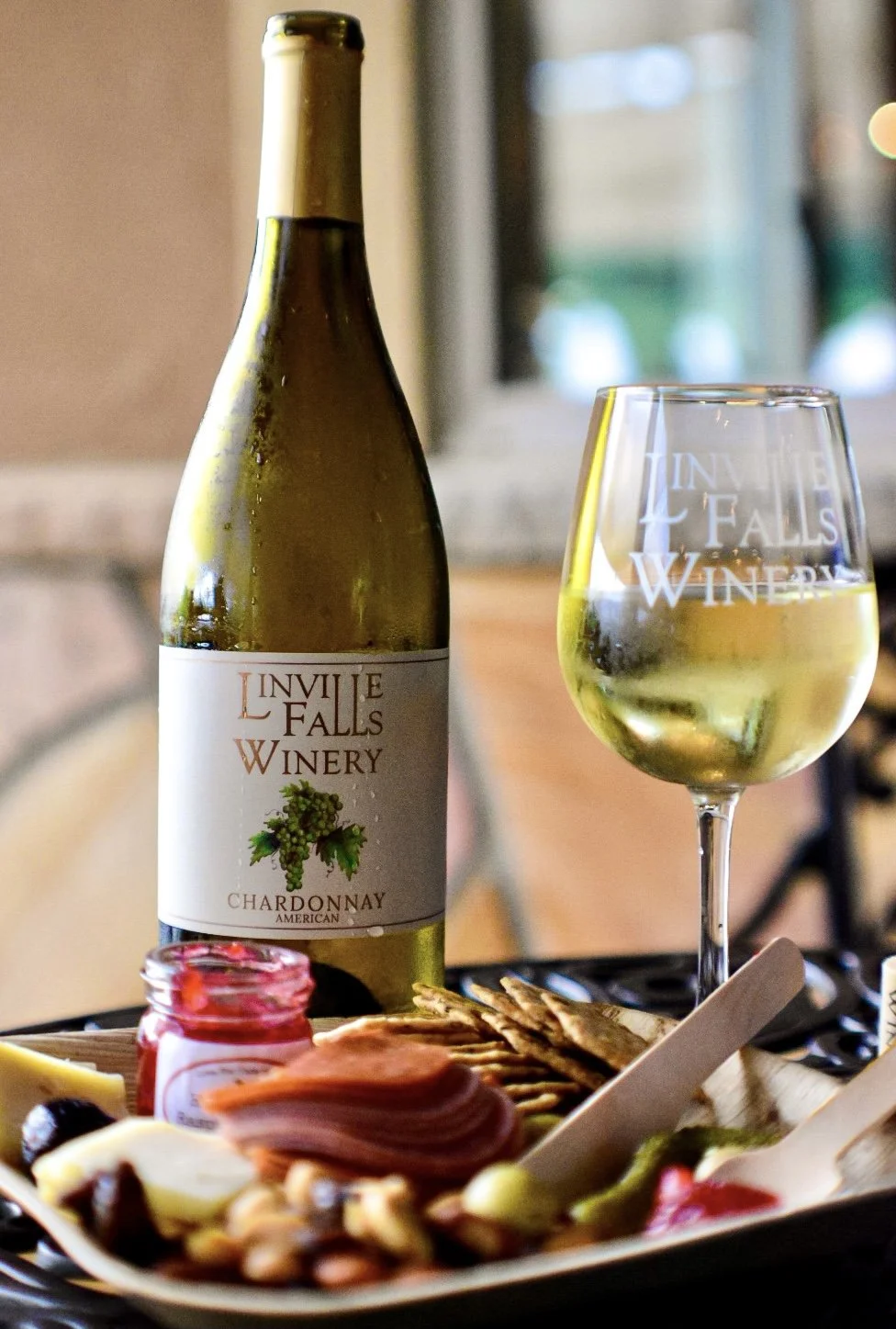 Yevette Lynn food and beverage photographer captures wine photography of Chardonnay bottle and filled glass beside charcuterie board in softly lit restaurant setting.