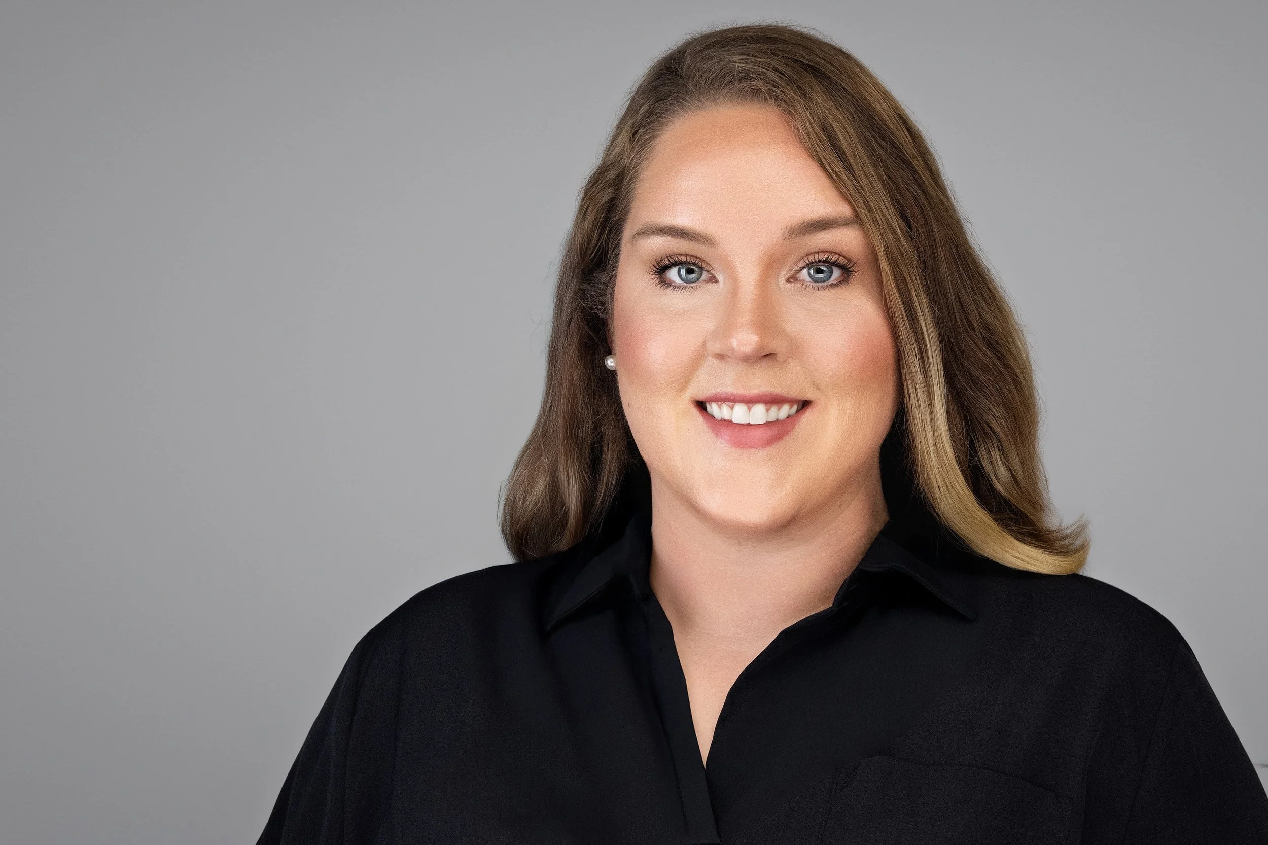 Yevette Lynn, professional photographer, captures a friendly studio headshot of a woman wearing a black top against a soft gray background.
