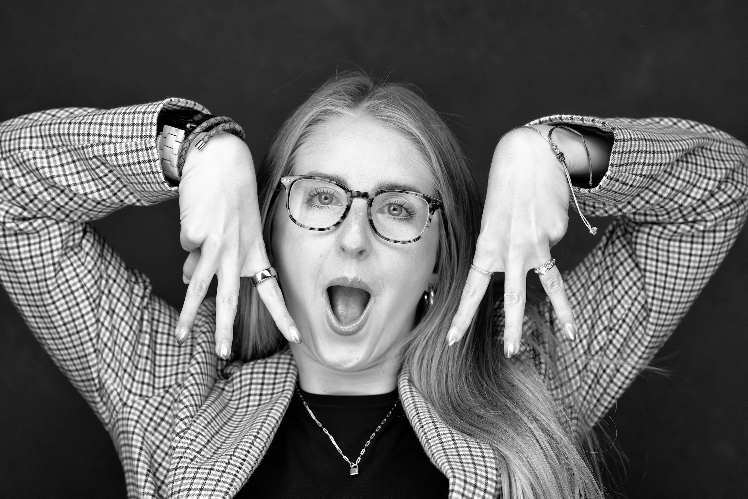 Playful headshot by Yevette Lynn, photographer capturing expressive portrait of woman with glasses using candid gesture for relaxed professional branding