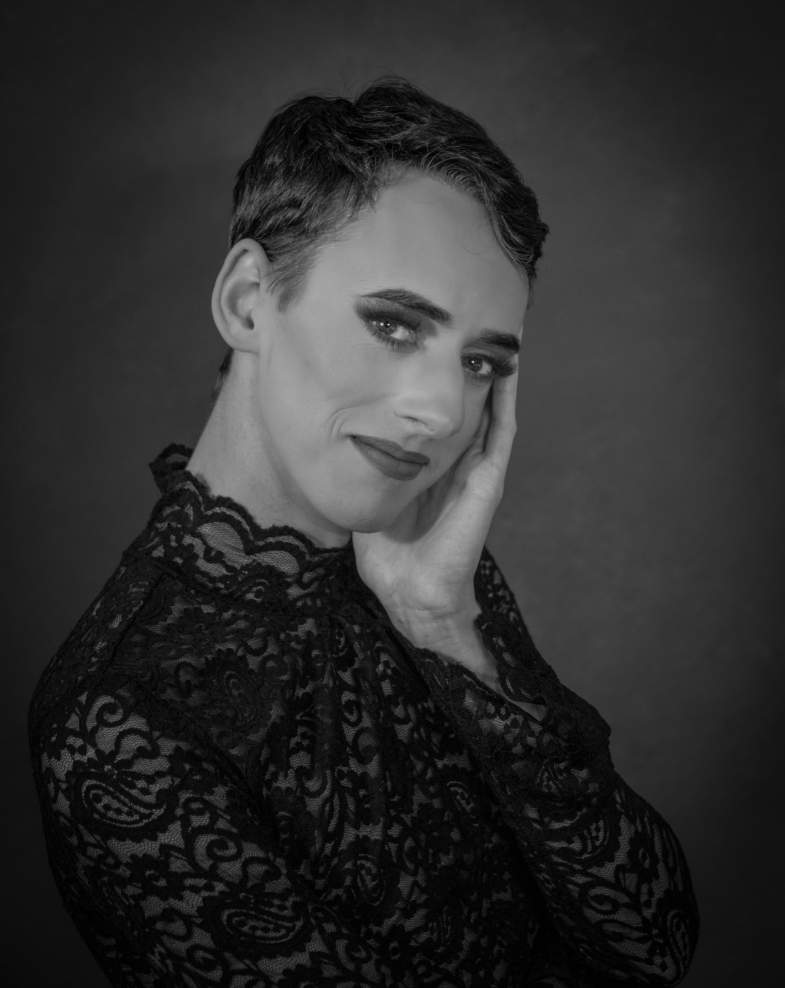 Yevette Lynn, brand photographer, captures a black and white studio portrait of a man in dark lace fashion with a soft, expressive pose.
