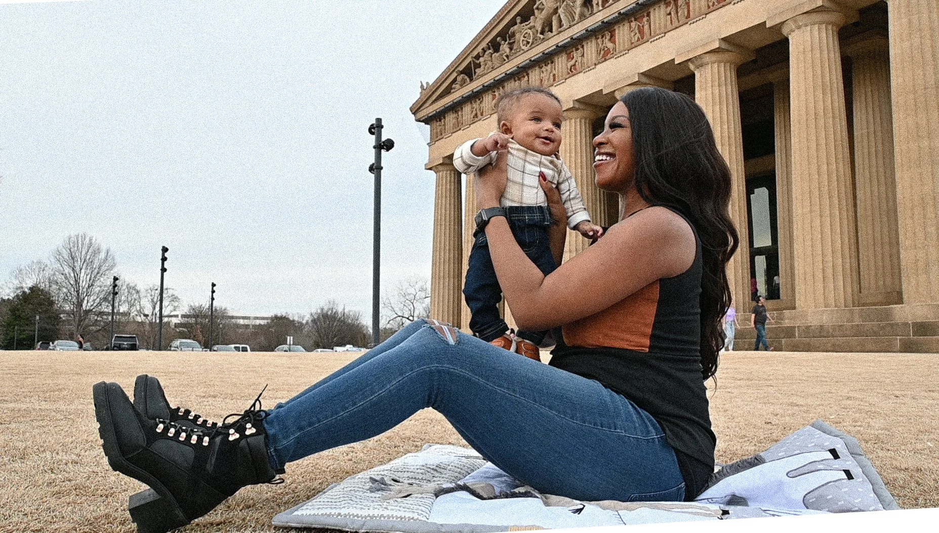 Yevette Lynn, lifestyle photographer, creates a black and white outdoor portrait of a mother lying on a blanket with her baby near classical columns.
