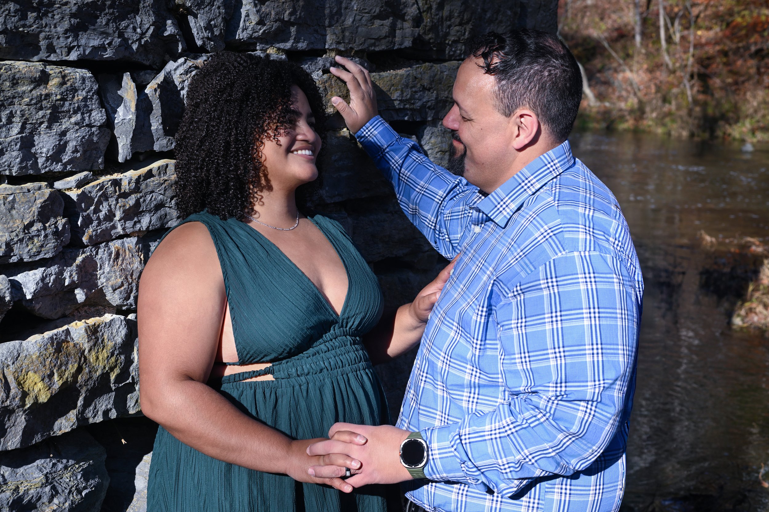 Yevette Lynn couples portrait photographer captures couple holding hands by stone wall near water, natural light outdoor portrait with intimate, relaxed connection.