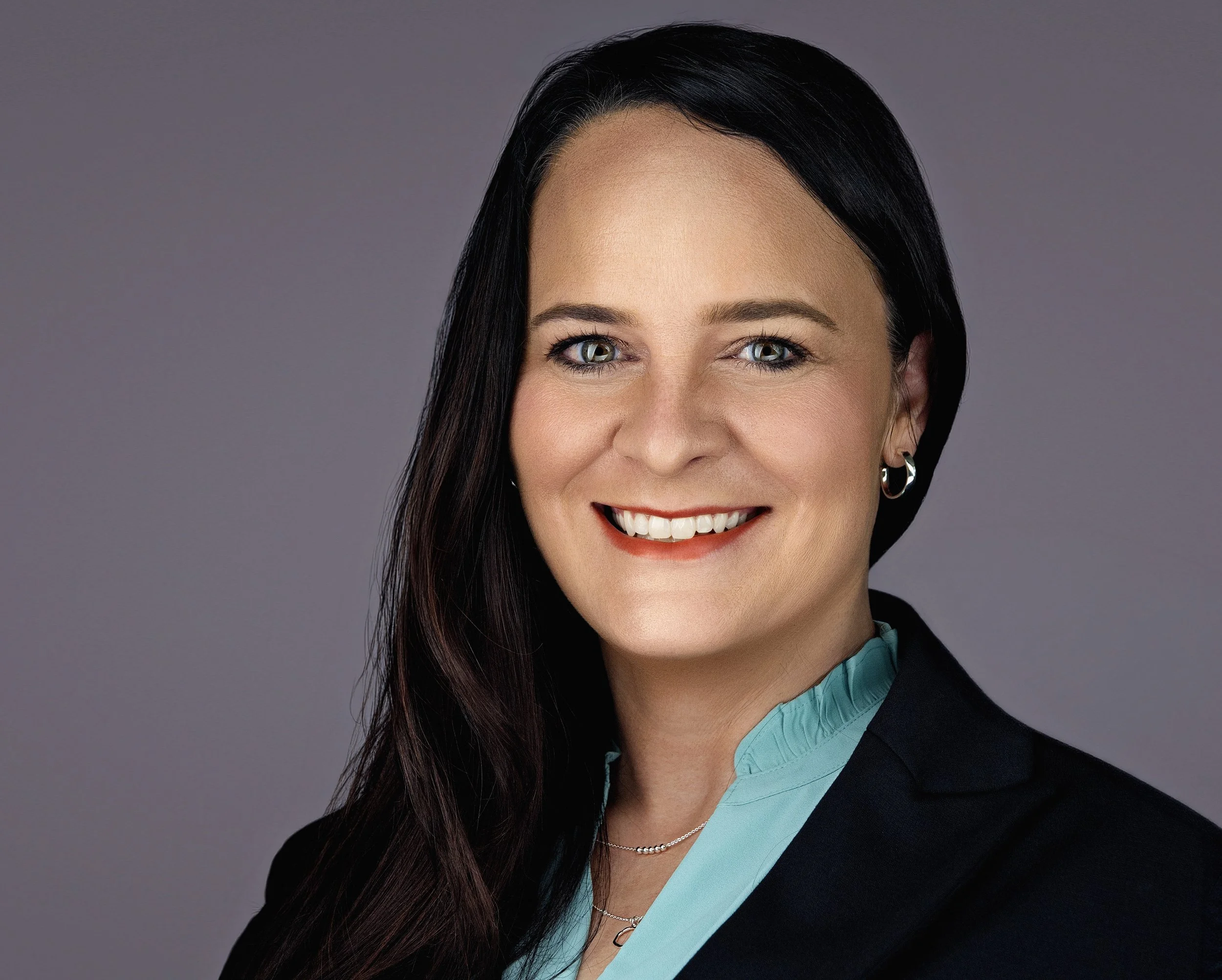 Professional studio headshot of a female corporate lawyer in business attire against a neutral gray background