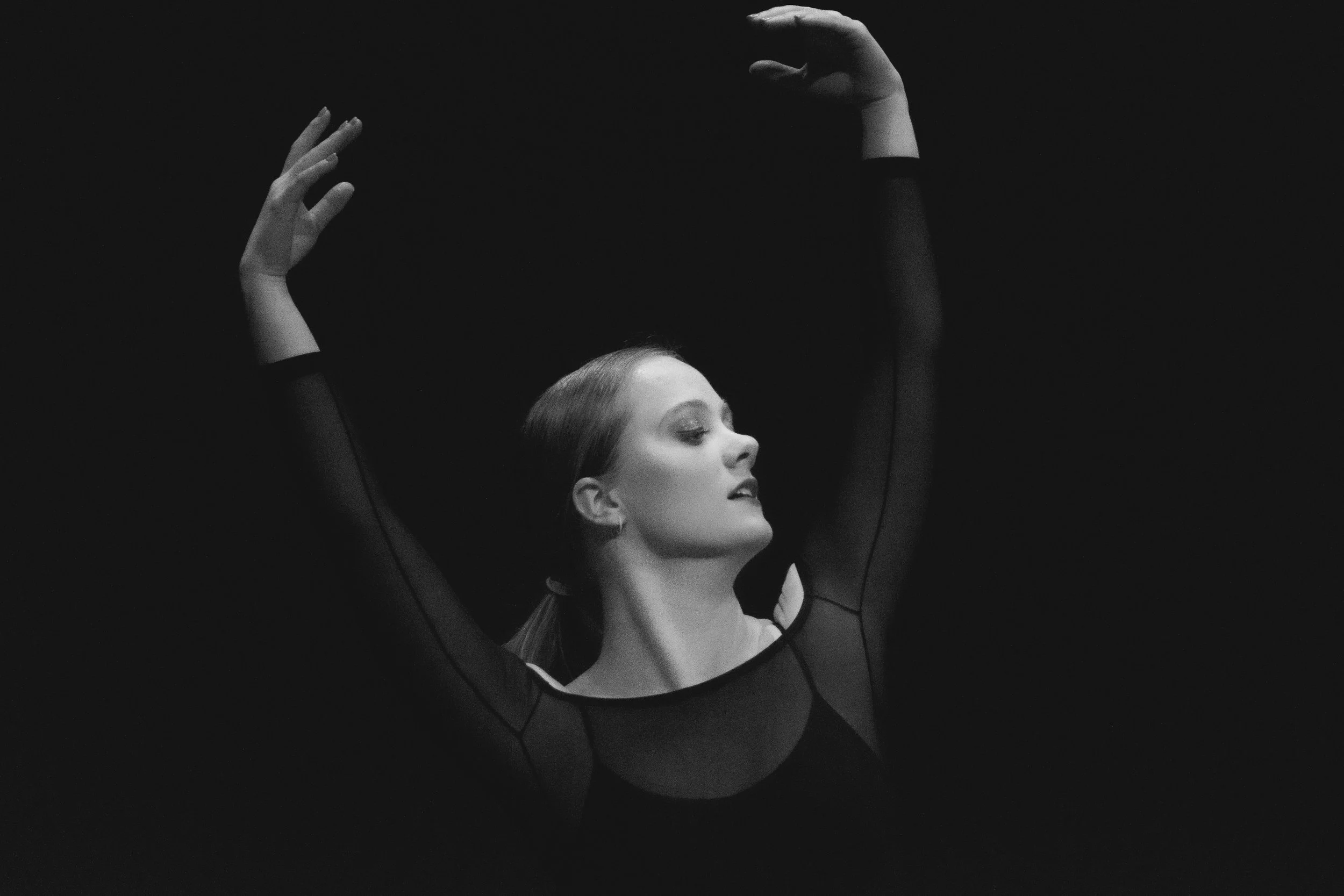 Yevette Lynn portrait photographer captures black and white studio dance portrait of woman with arms raised gracefully, expressive movement against dark background.