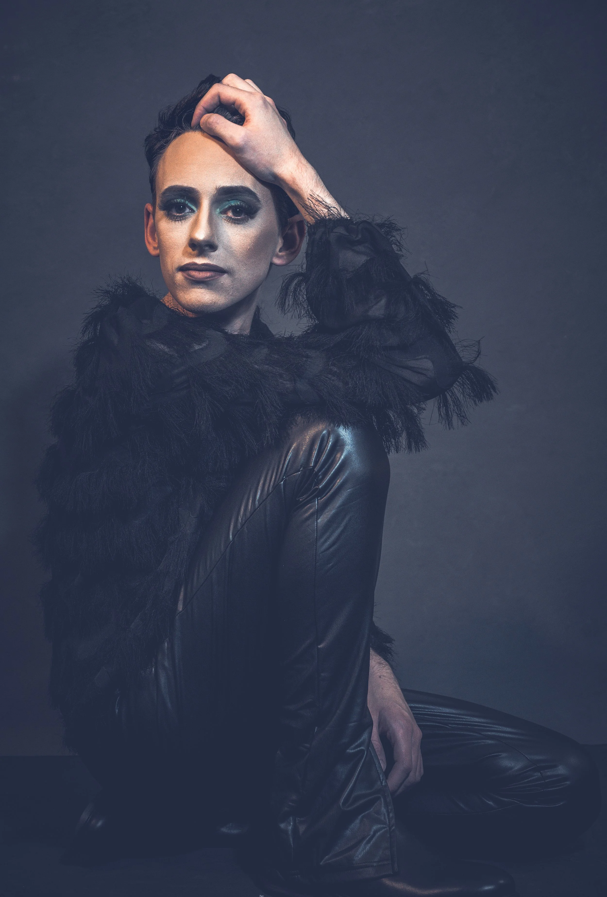 Yevette Lynn, brand photographer, captures a dramatic studio portrait of a man in dark fashion with feathered details and a strong, expressive pose.