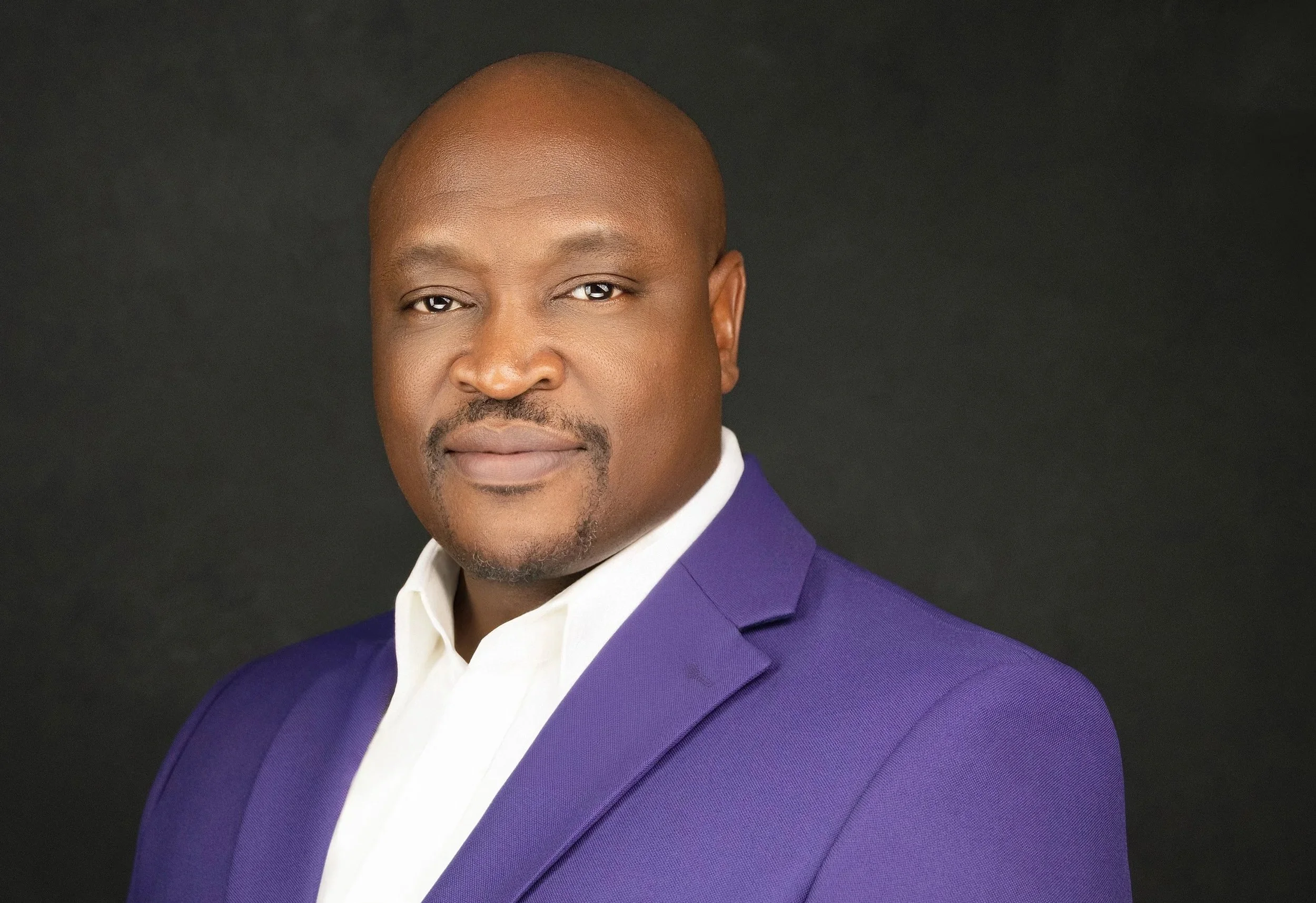 Yevette Lynn, professional photographer, creates a professional studio headshot for business branding, featuring a man in a purple blazer against a dark background.