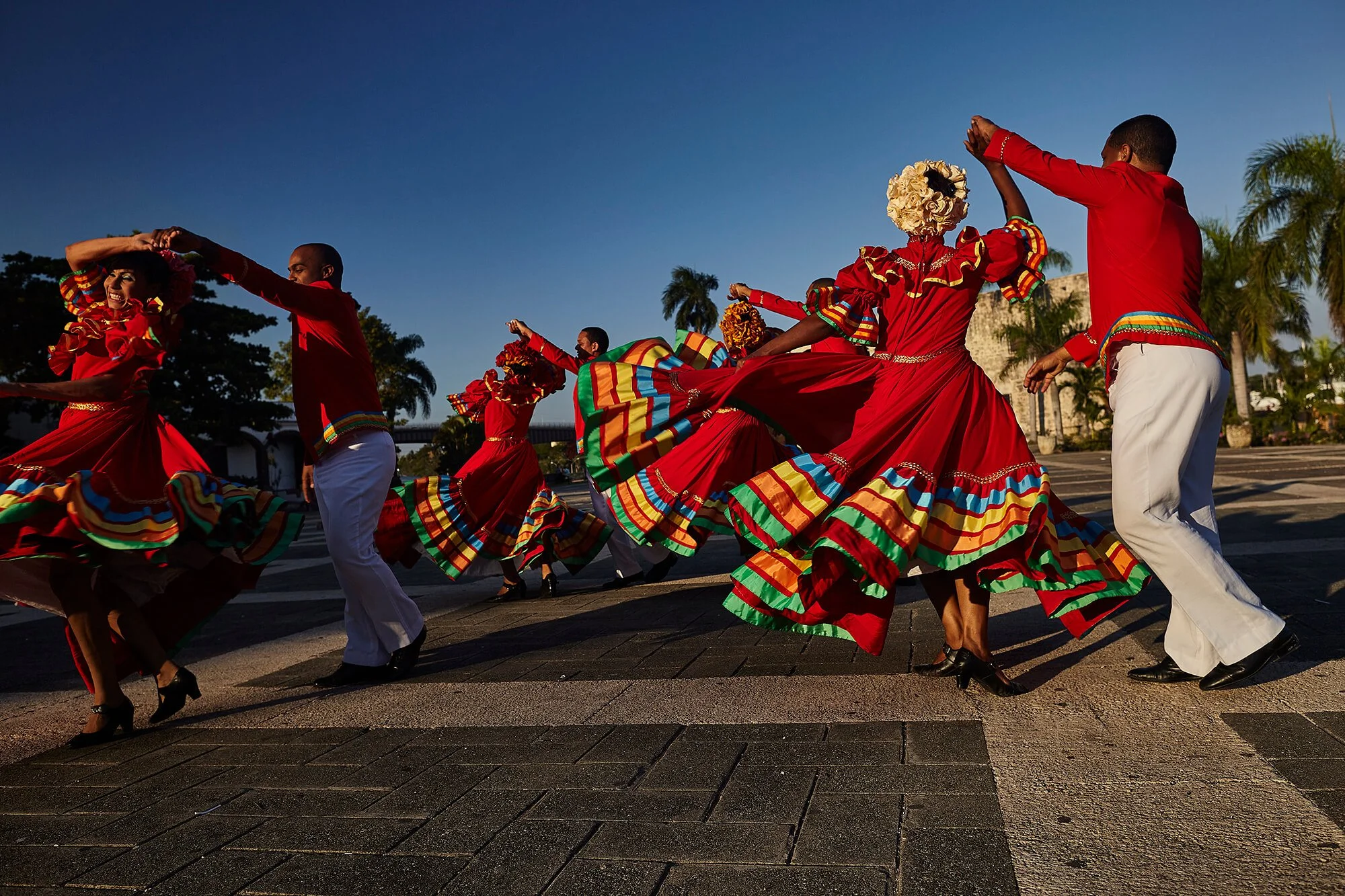Group of dancers in colorful traditional costumes performing outdoors during sunset.