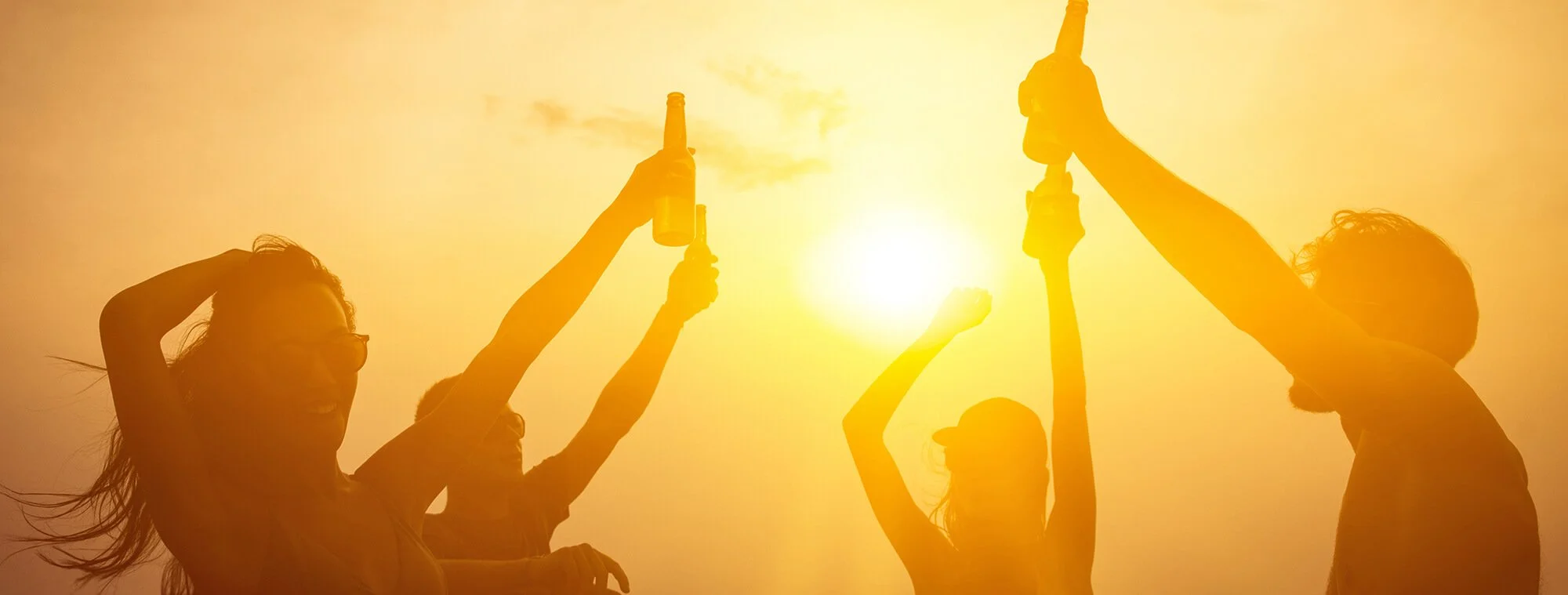 A group of people raising their drinks in the air at sunset, celebrating outdoors.