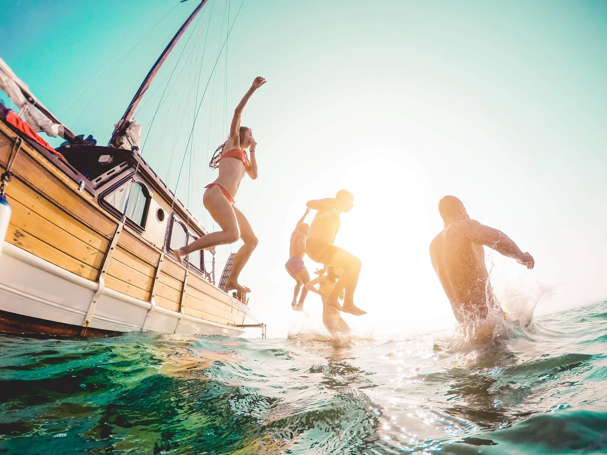 People jumping off a boat into the water on a sunny day.