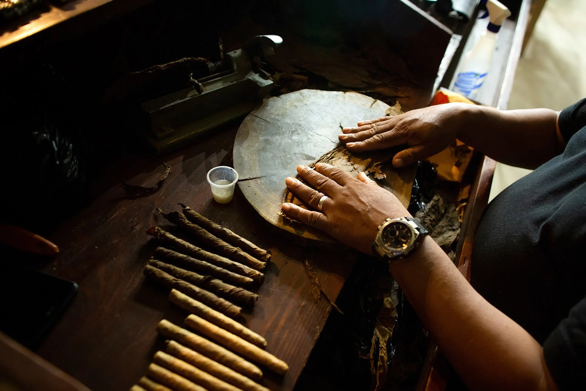 Person rolling cigar wrappers on a wooden work surface with cigar cigarellos laid out next to their hands.