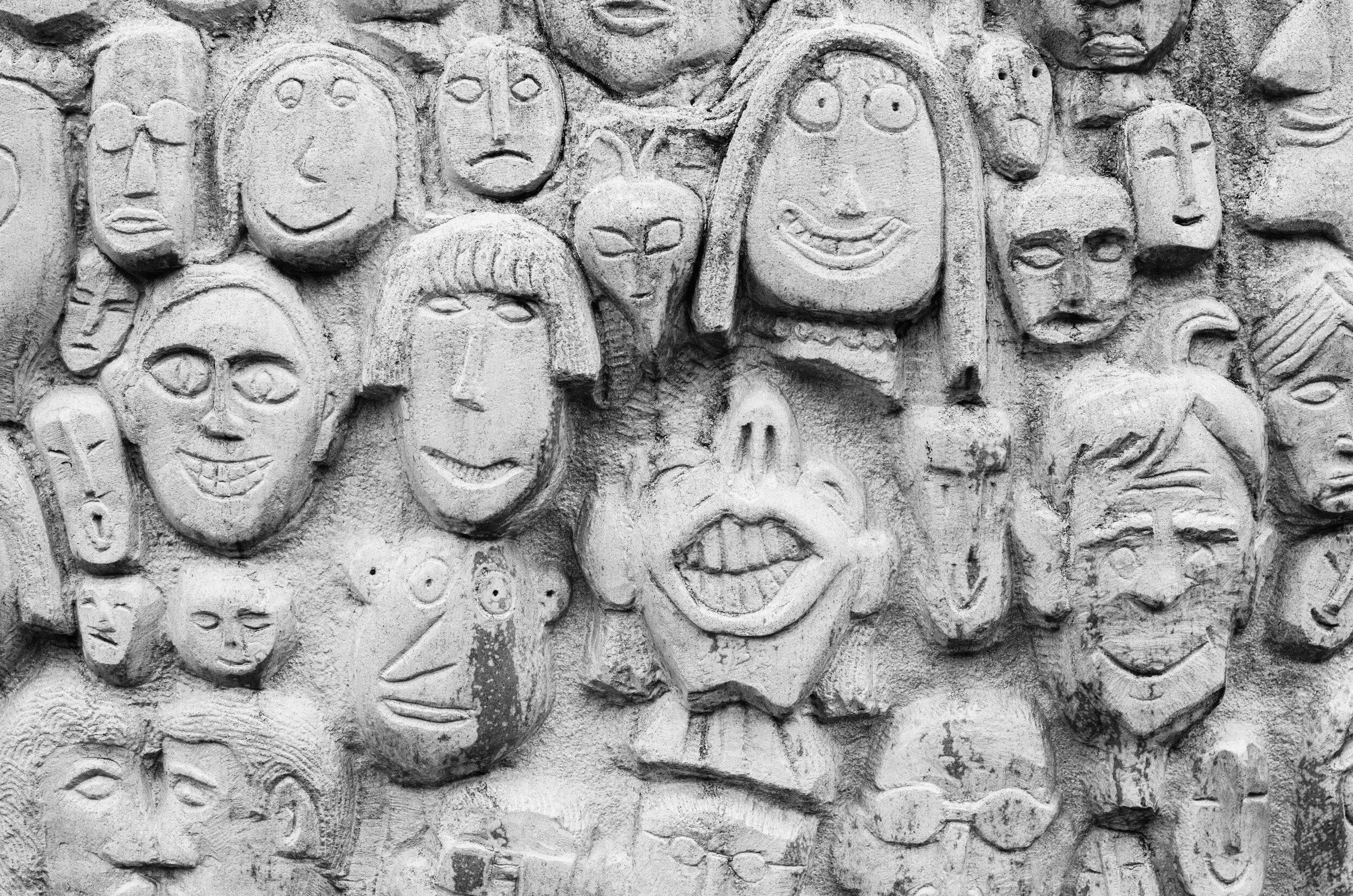Wall of stone with different faces carved into it.