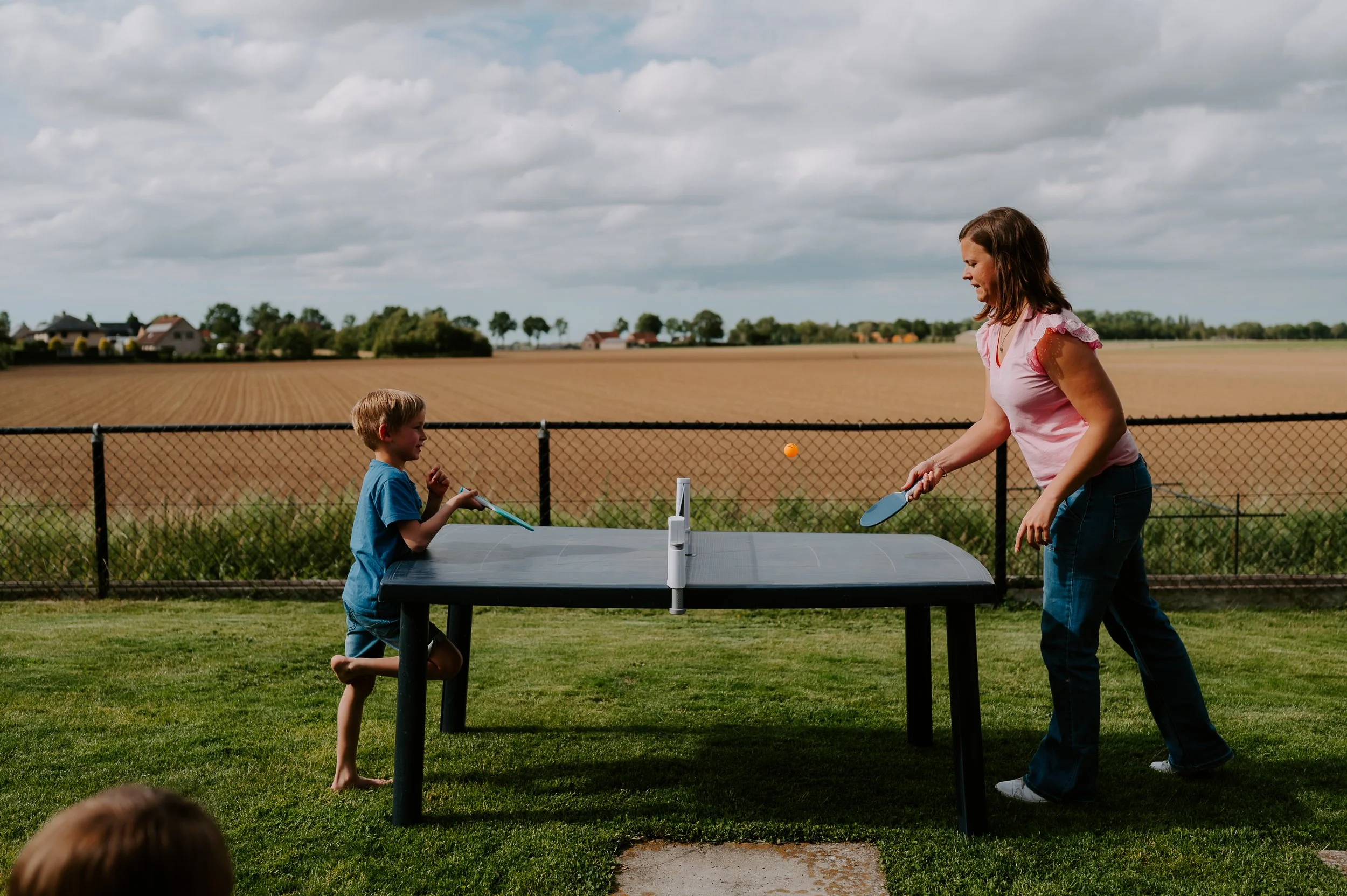 mama en zoon spelen ping pong in de tuin tijdens een gezinsshoot.