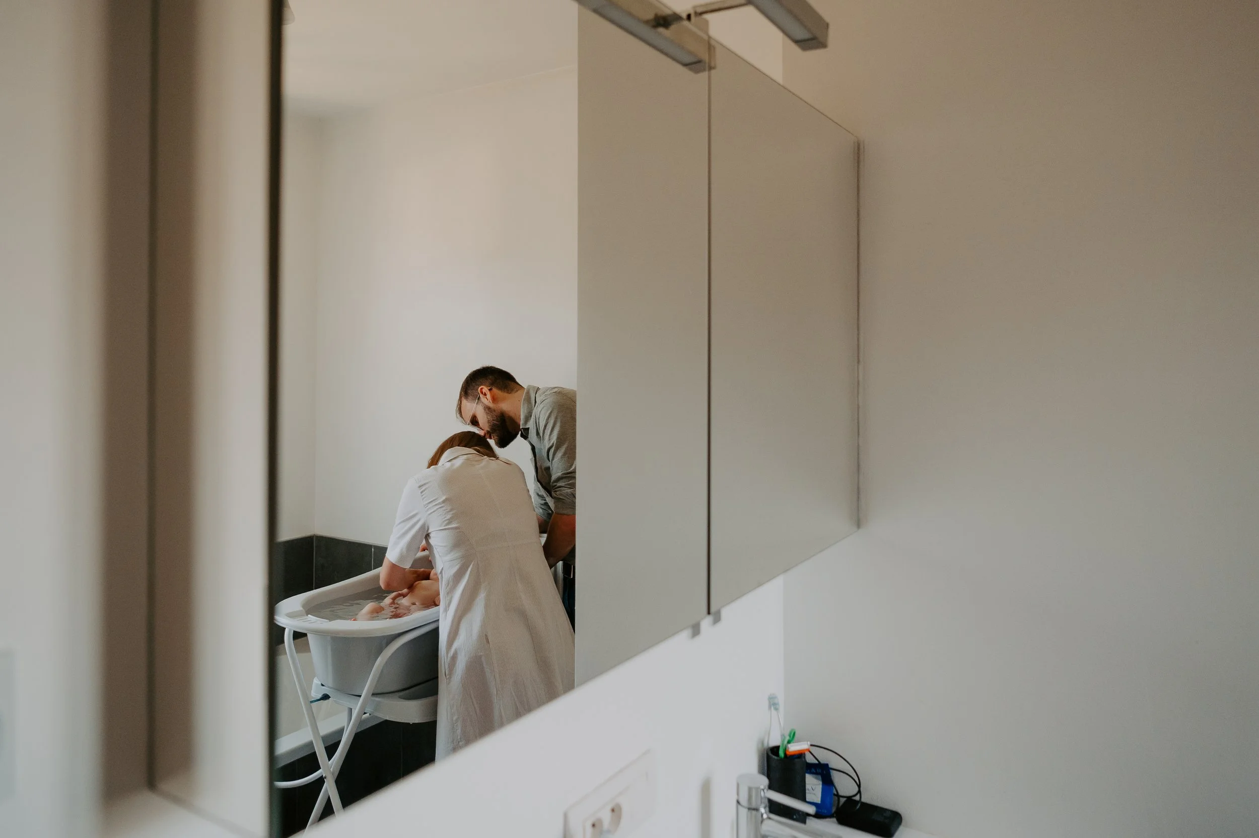 een gezinsfoto gemaakt in de spiegel van mama en papa die baby wassen