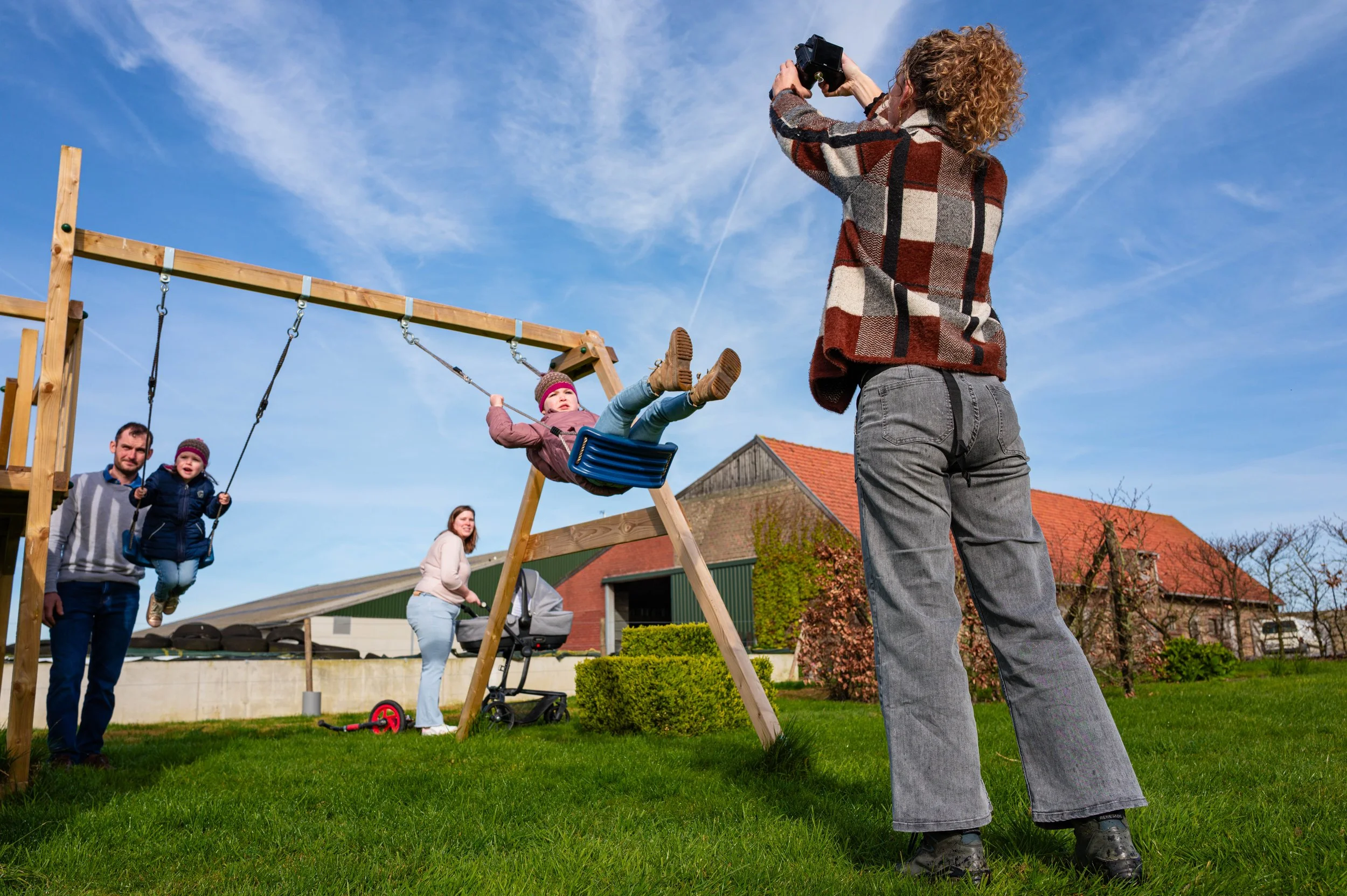 gezinsfoto van mama en papa die kijken naar de kindjes die spelen op de schommel 