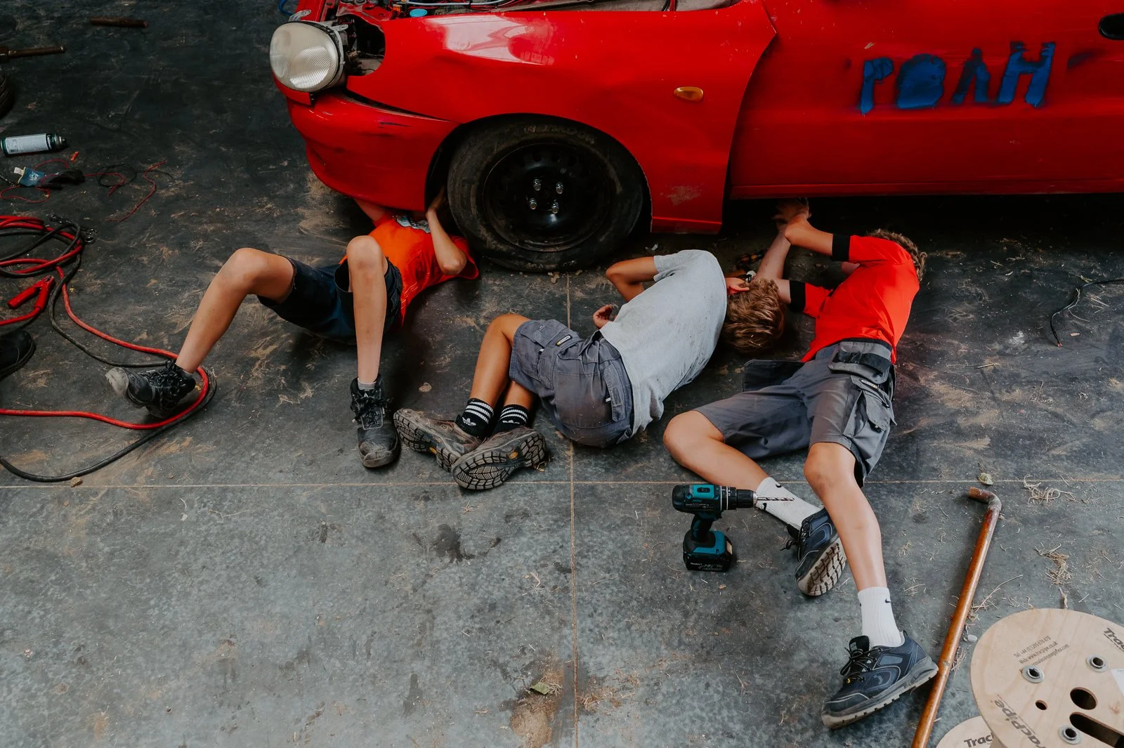 3 kinderen liggen onder de auto op de vloer van de loods van dit gezin