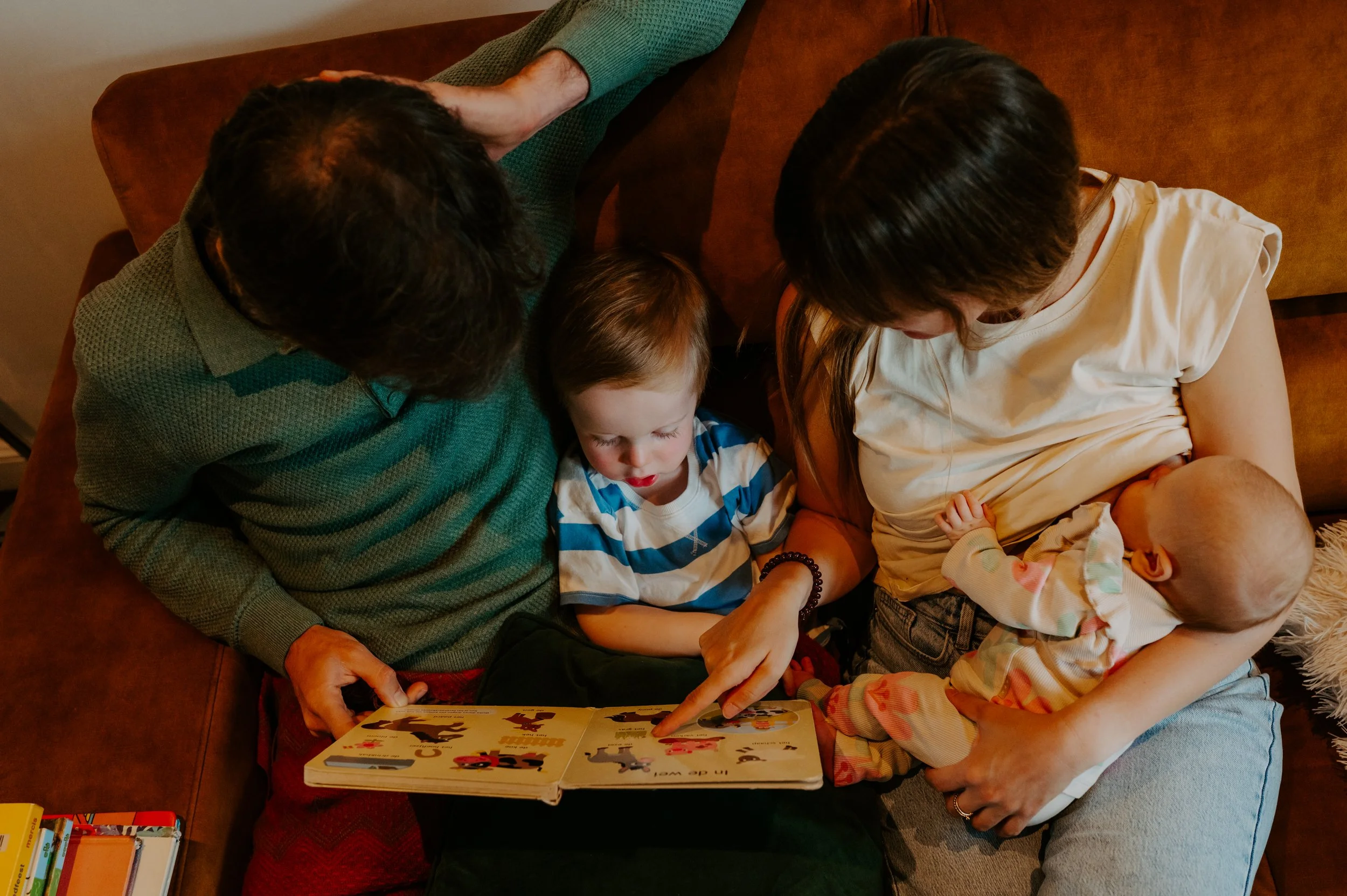 papa en mama lezen voor in de zetel en klein baby zusje drinkt borstvoeding