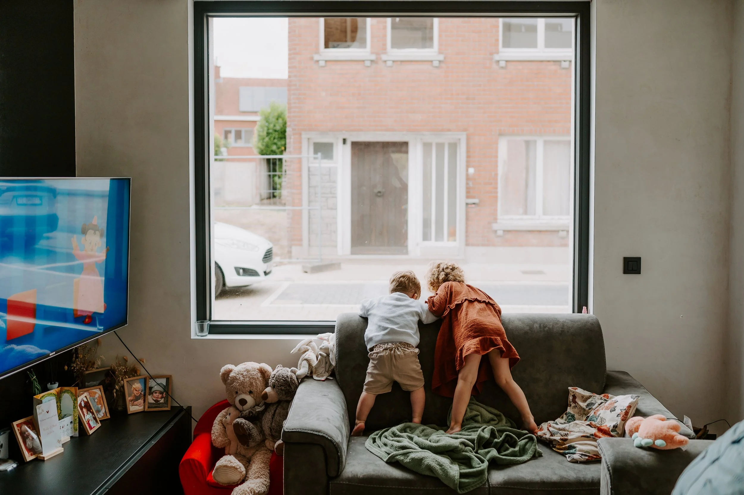 2 kindjes wachten papa op aan het raam tijdens een gezinsshoot