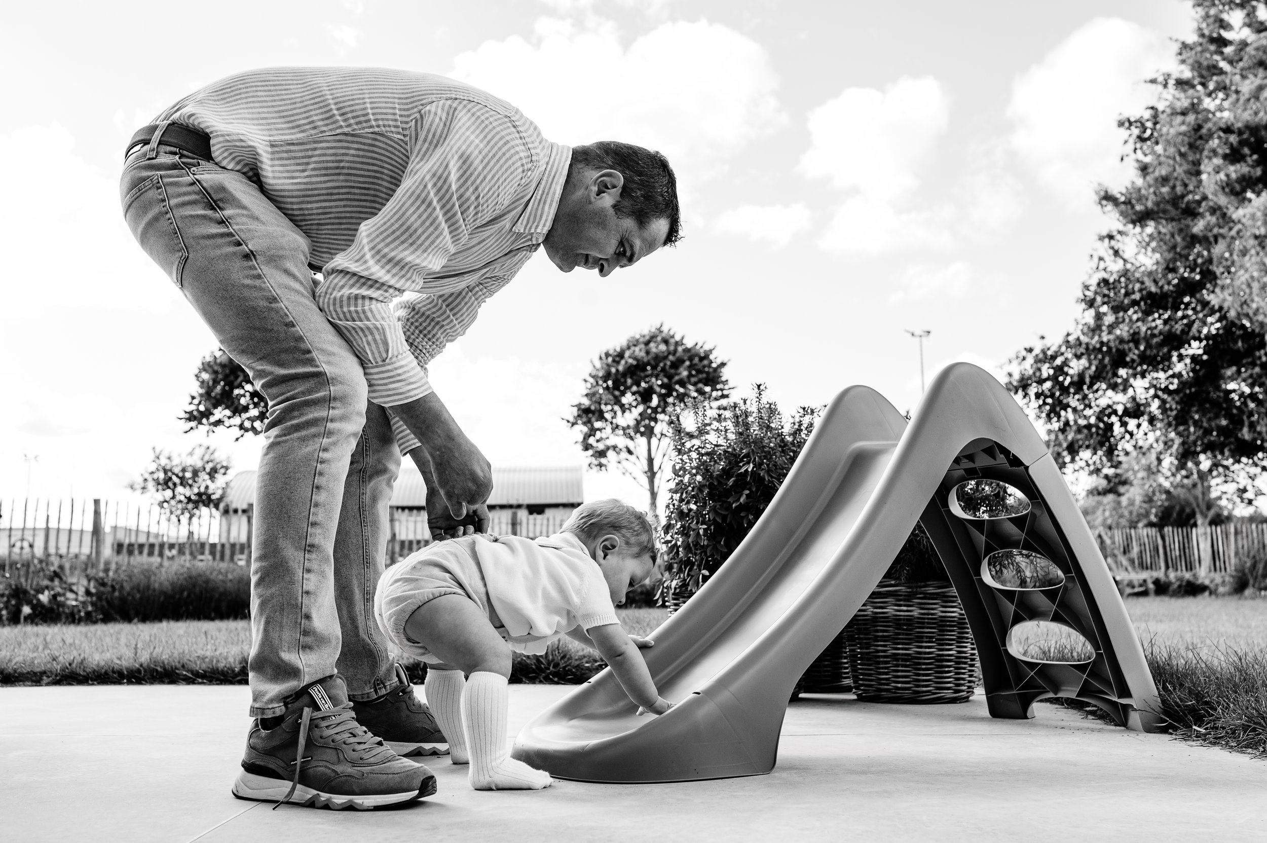 een gezinsfoto waarop papa speelt met zijn 1jarig zoontje op de glijbaan