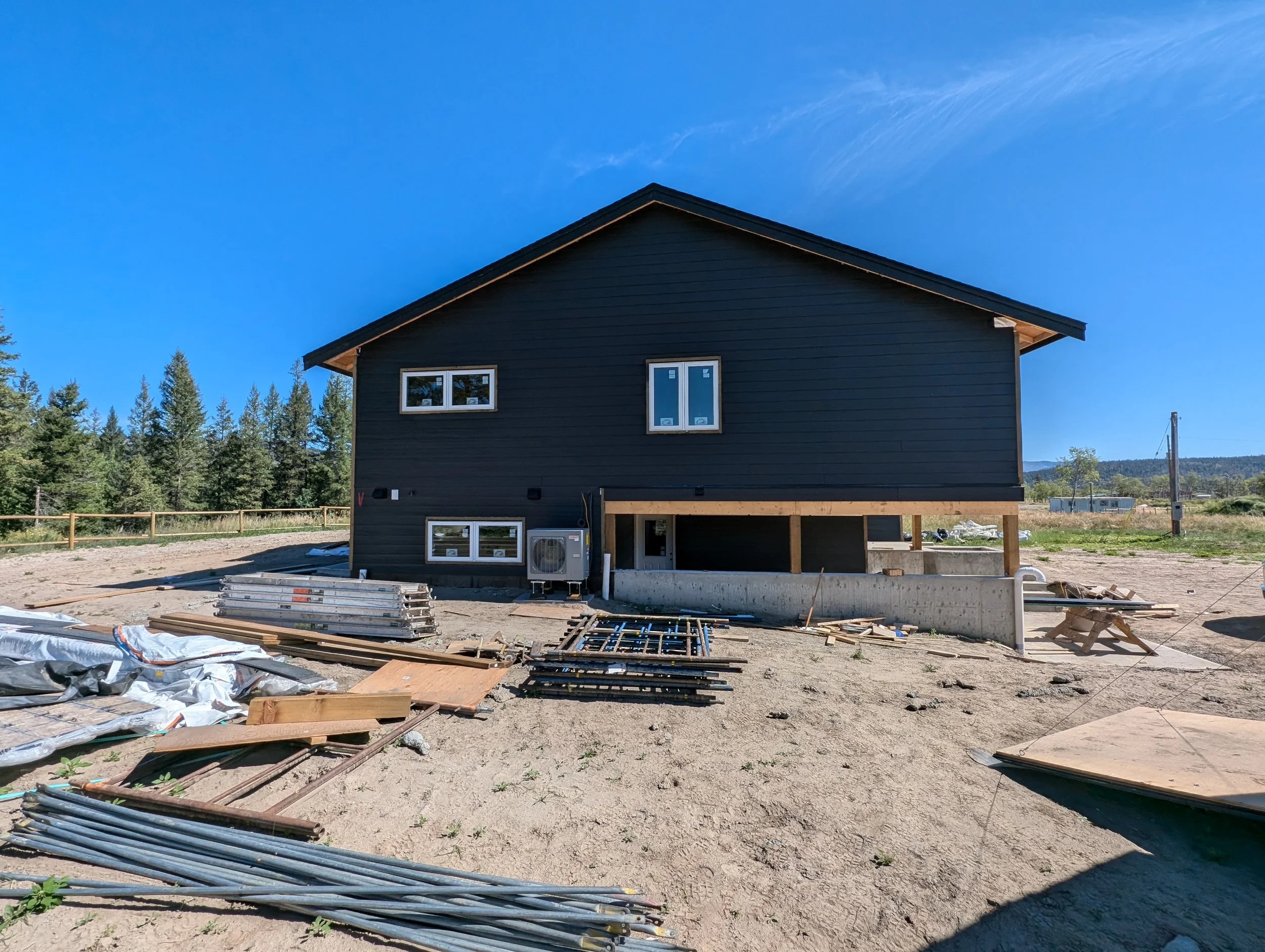 A house under construction with dark exterior siding, multiple windows, an unfinished porch area, and a saw on a stand. Professional siding installation, replacement, and exterior renovations in Williams Lake and the Cariboo Region. 