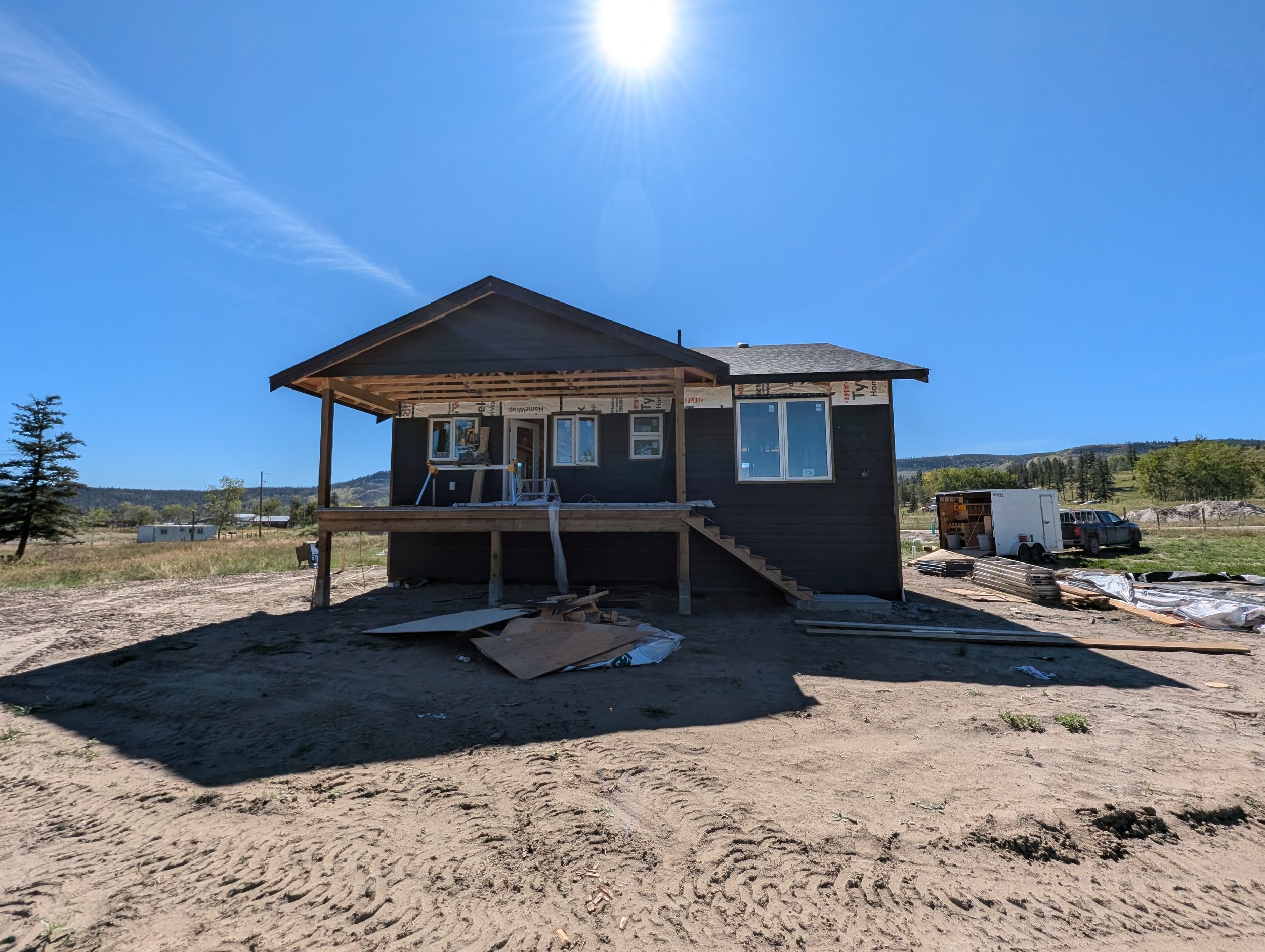 A house under construction with dark exterior siding, multiple windows, an unfinished porch area, and a saw on a stand. Professional siding installation, replacement, and exterior renovations in Williams Lake and the Cariboo Region. 