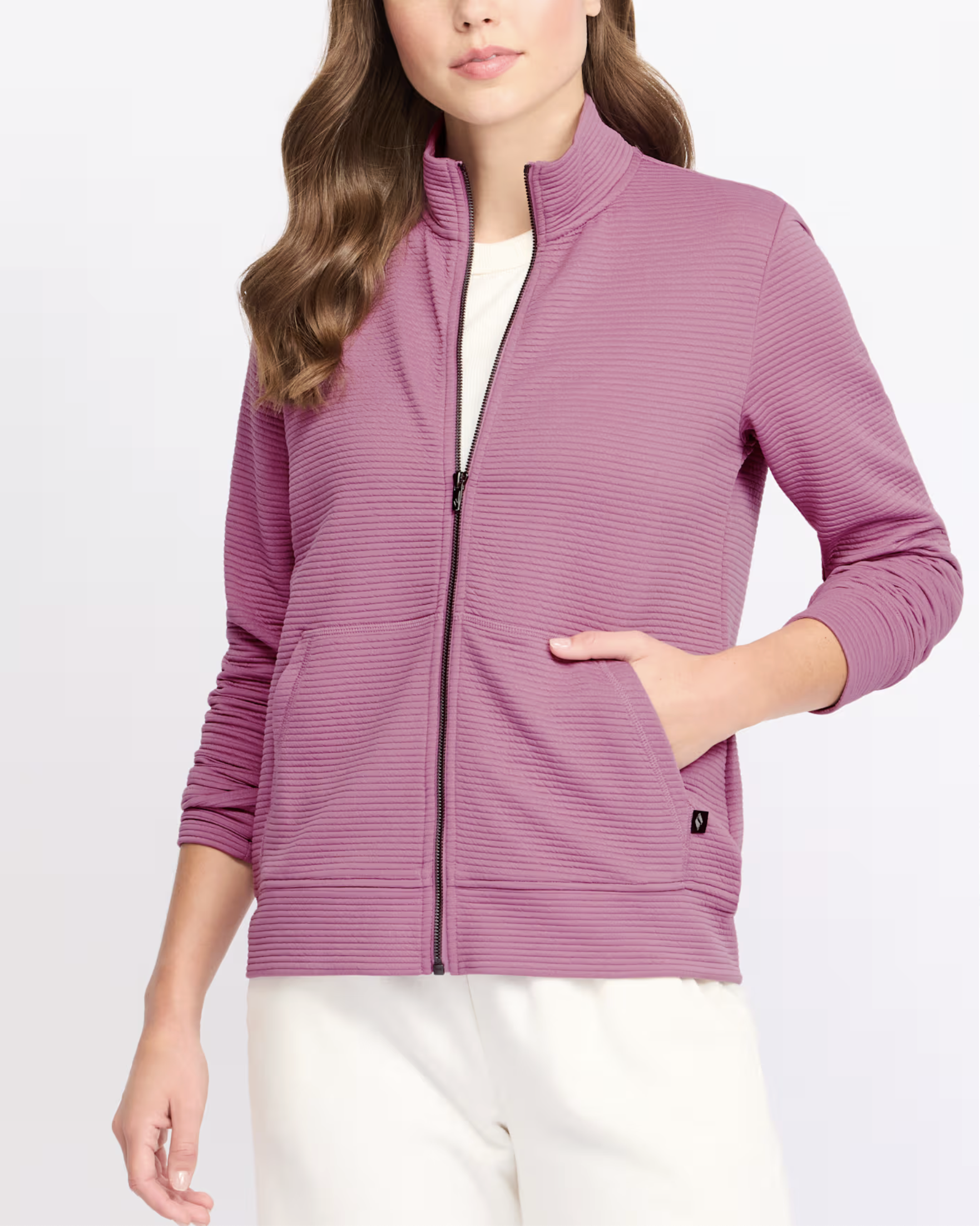 Woman wearing a pink textured zip-up jacket with a high collar and cream-colored pants, standing against a white background.