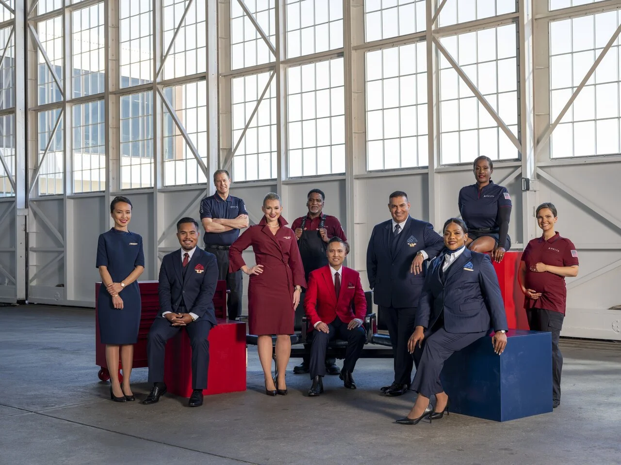 Group of diverse airline crew members and staff posing inside an aircraft hangar with large windows and metal framework.