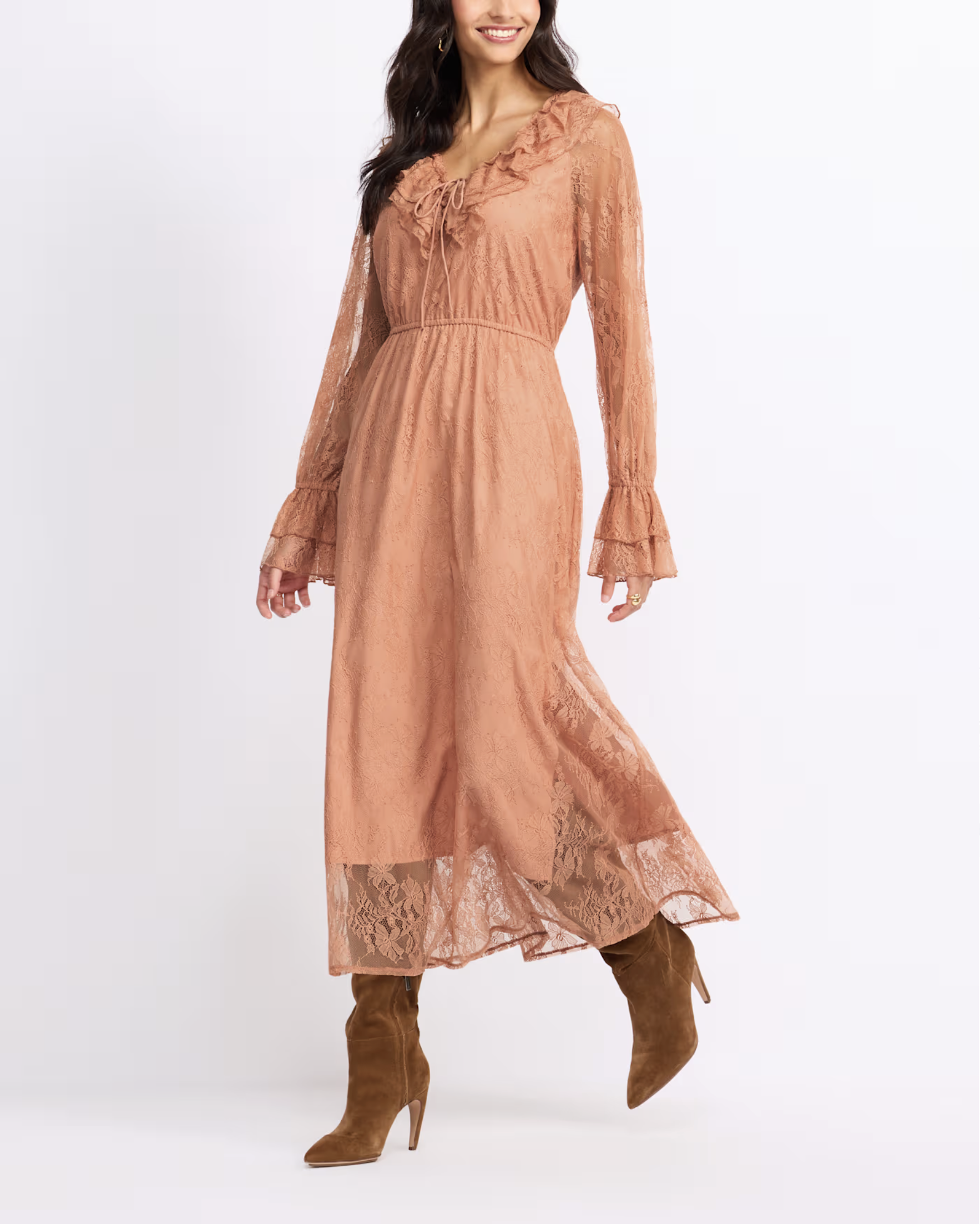 Woman wearing a long peach-colored lace dress with long sleeves and ruffle details, paired with brown high-heeled boots.