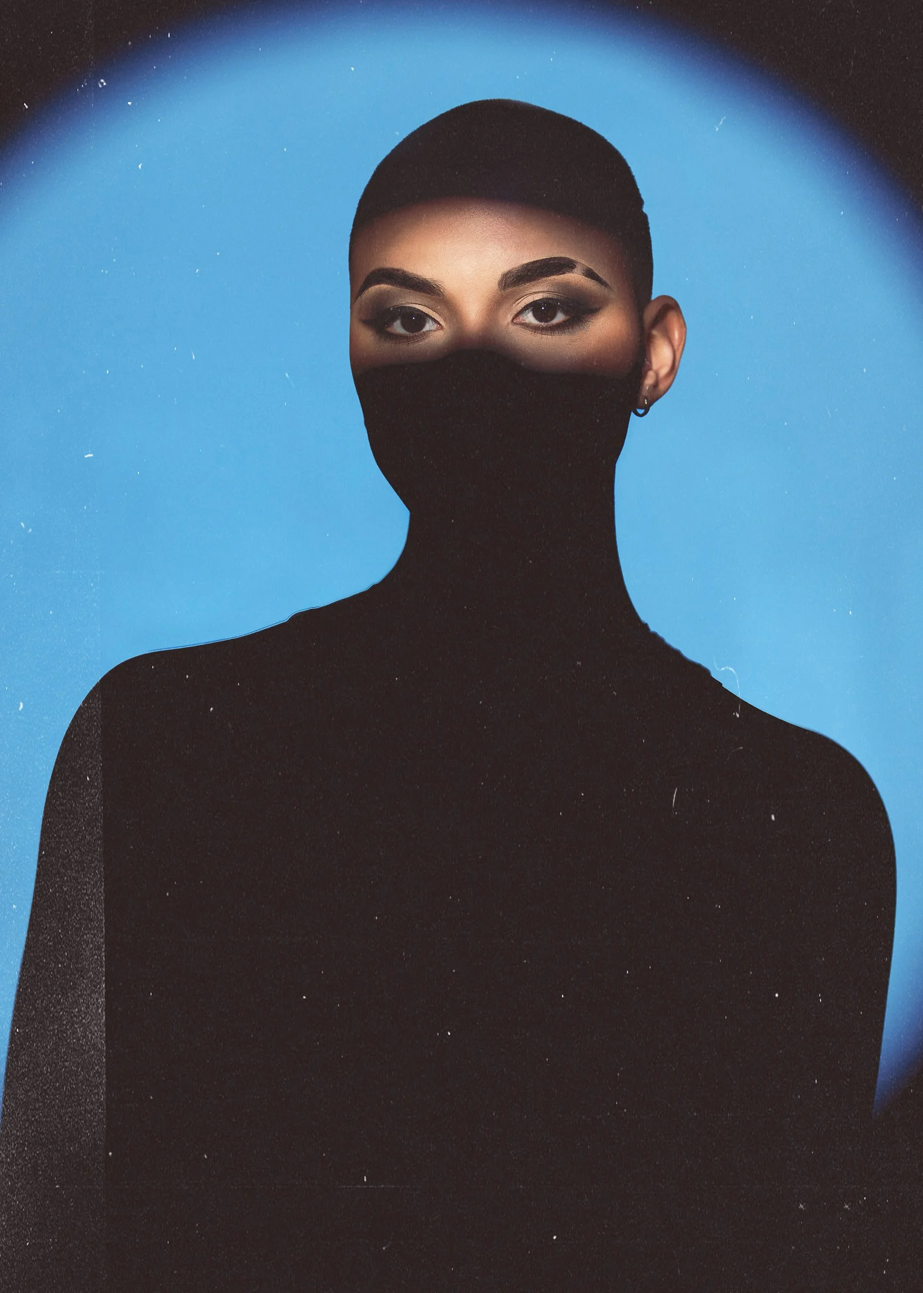 A woman with short hair and makeup, wearing a black high-neck top and a black face mask, against a blue background.