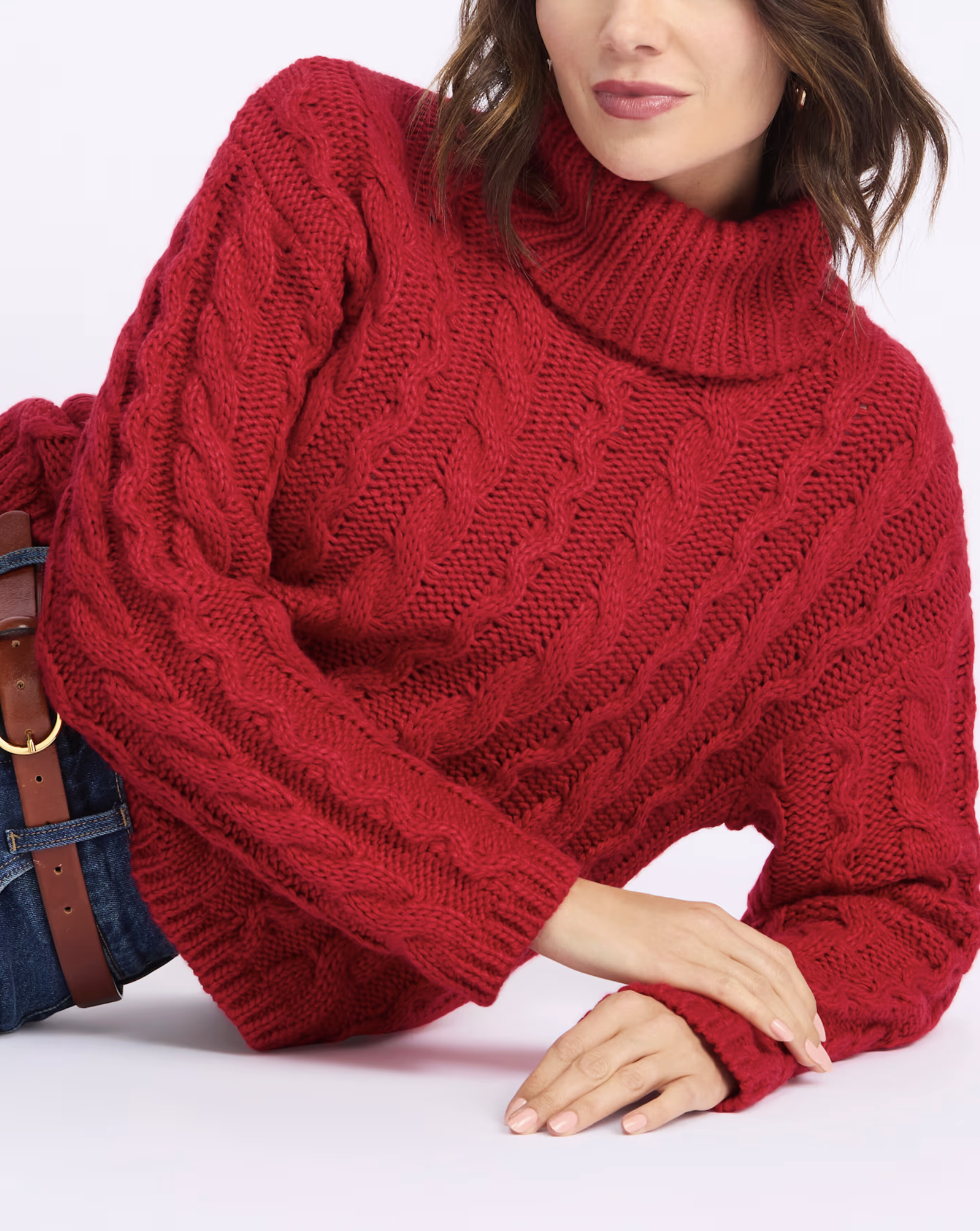 Woman wearing a red cable-knit turtleneck sweater with her arms crossed, against a white background.