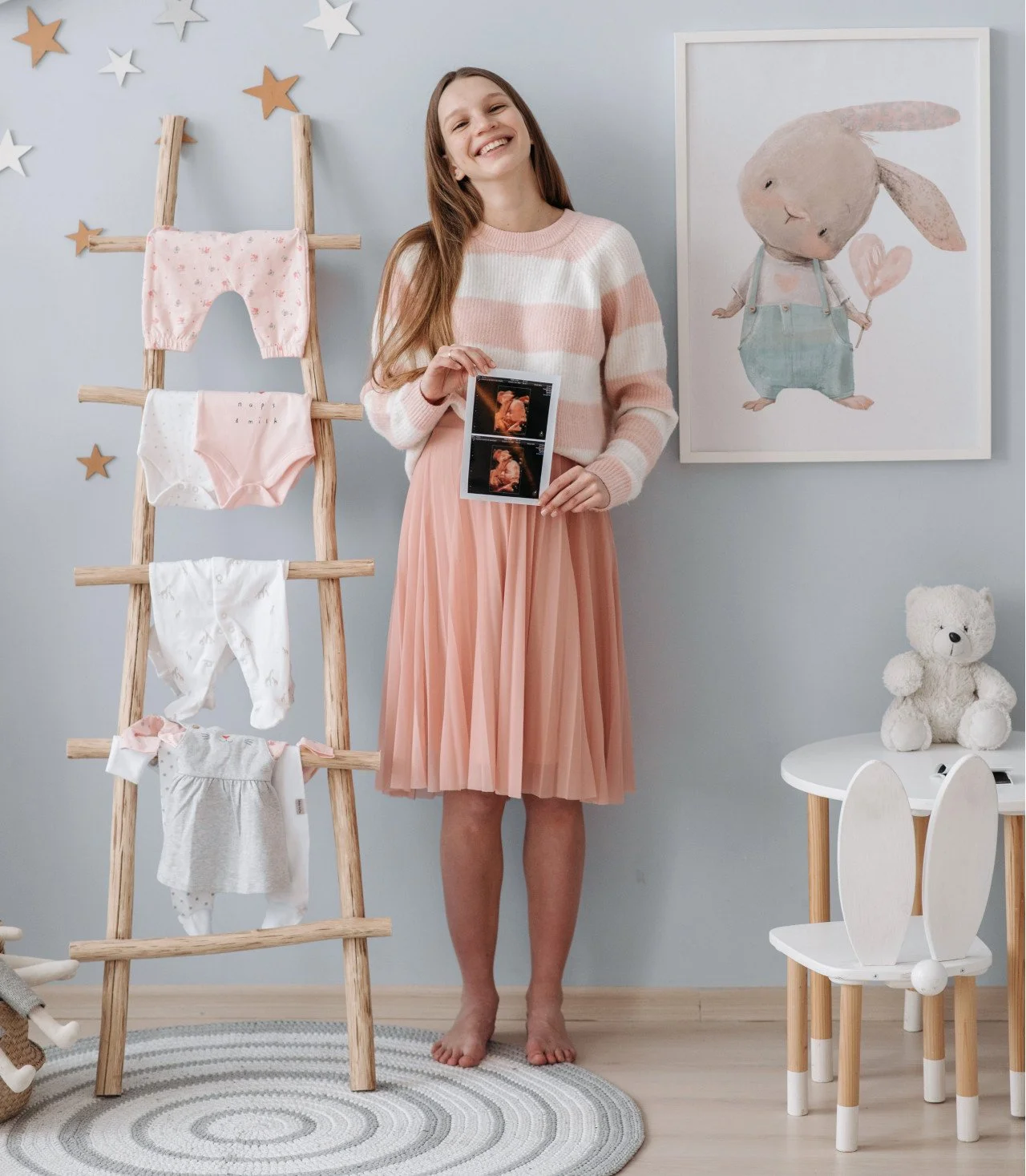 Pregnant mom wearing maternity clothes standing in decorated baby nursery.