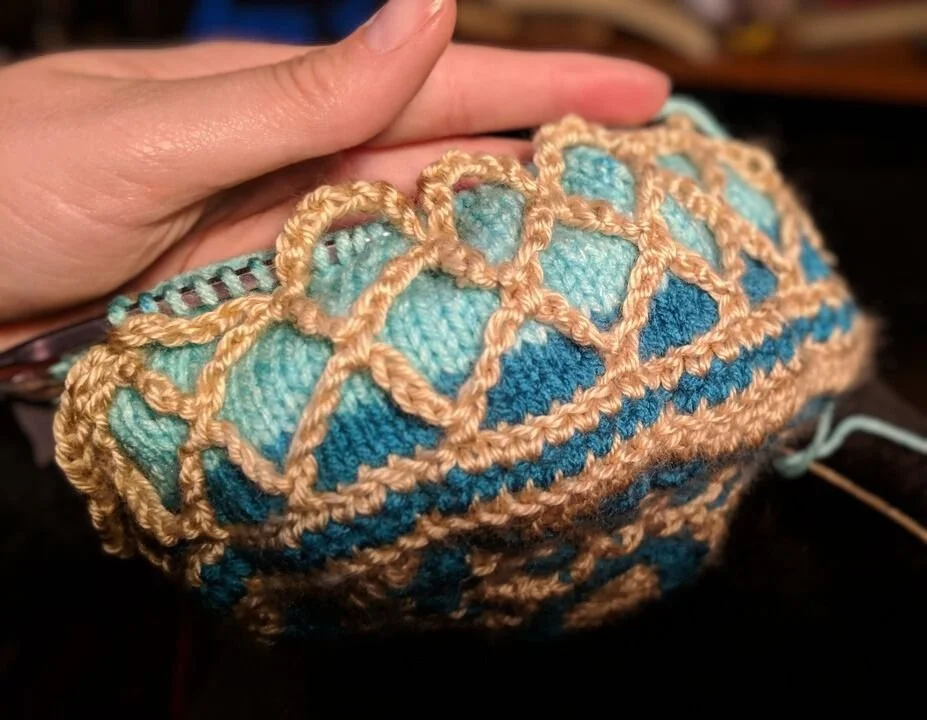 Close-up of a hand holding a crocheted item with intricate blue and peach-colored yarn patterns.