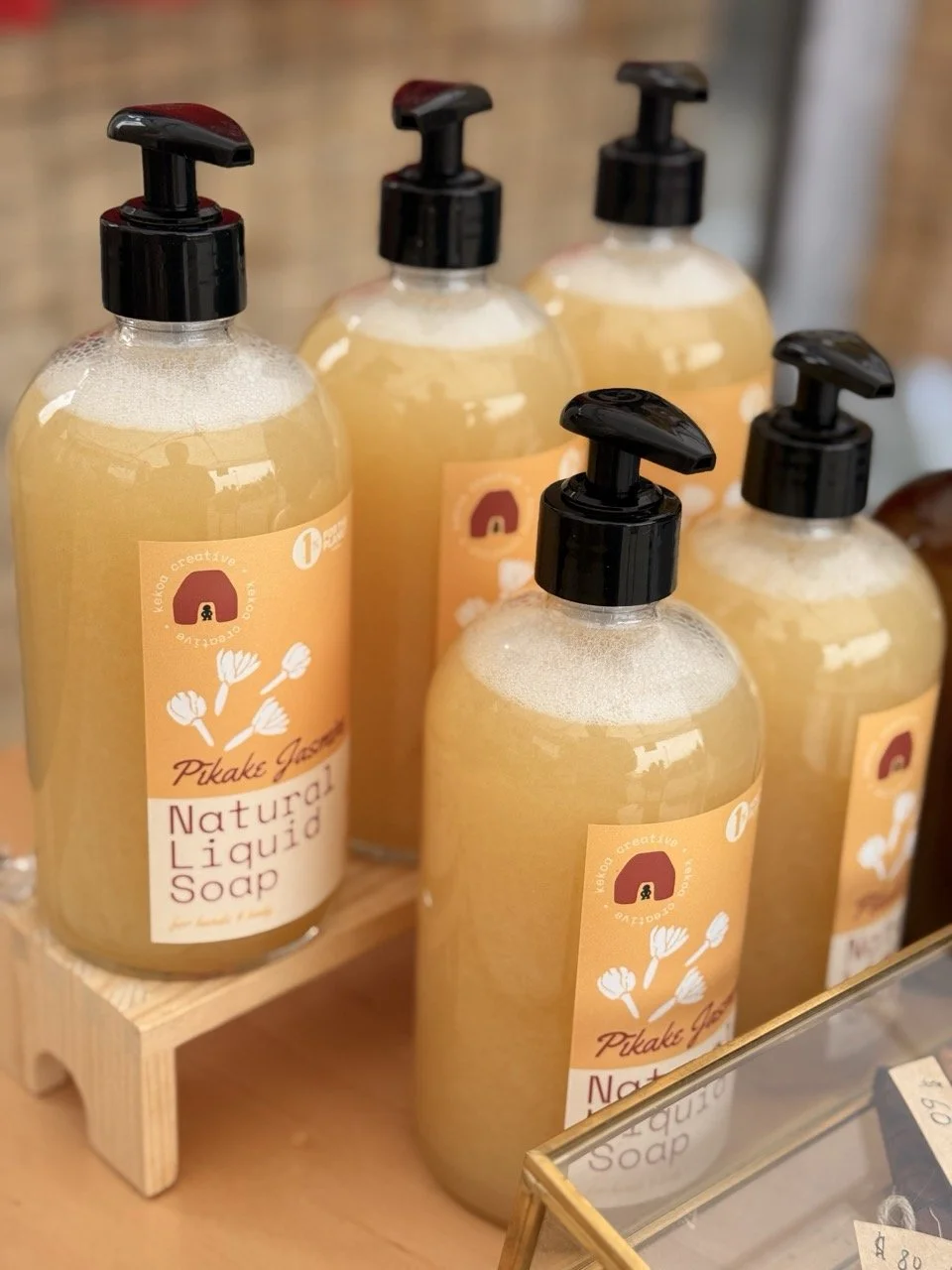 collection of Pīkake Jasmine natural liquid soaps in a clear flint glass pump bottle with Hawaiian Kukui nut oil by Kekoa Creative at a selling event.