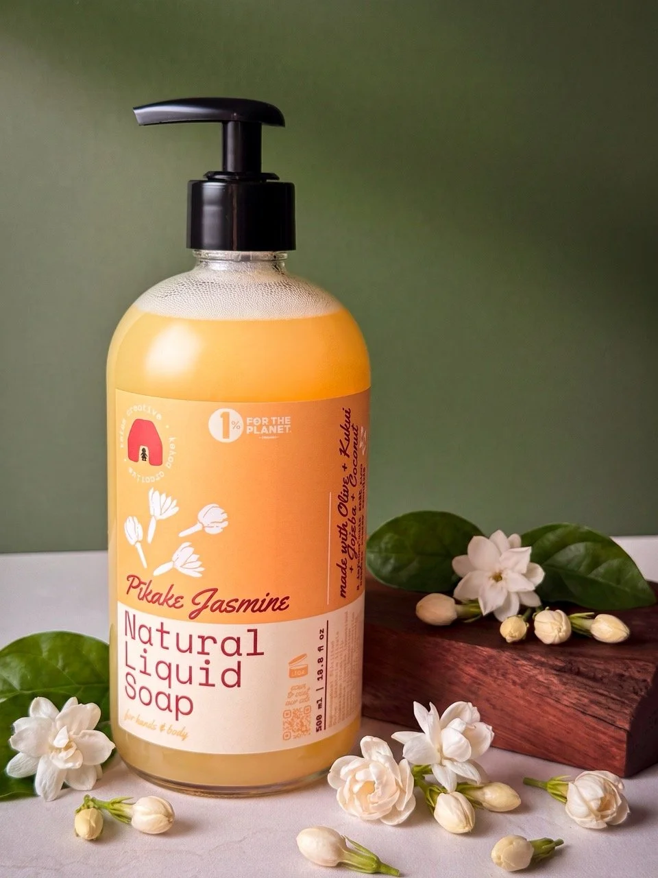 Pīkake Jasmine natural liquid soap in a clear flint glass pump bottle with Hawaiian Kukui nut oil by Kekoa Creative with pīkake jasmine flowers all around the display.