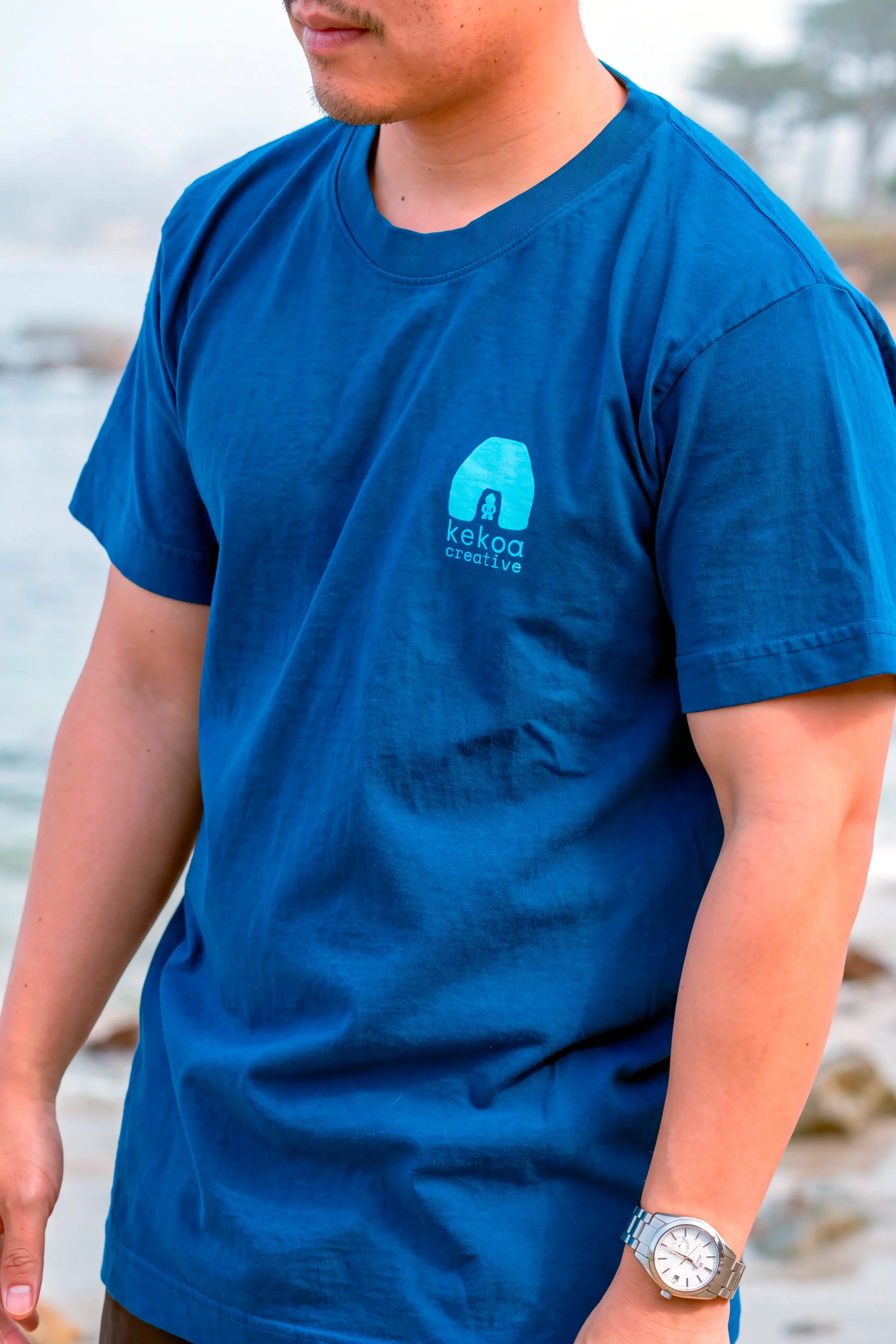 Model wearing unisex Moana Blue Kumulipo i ke Kohola short sleeve reclaimed cotton graphic tee with chest logo by Kekoa Creative.
