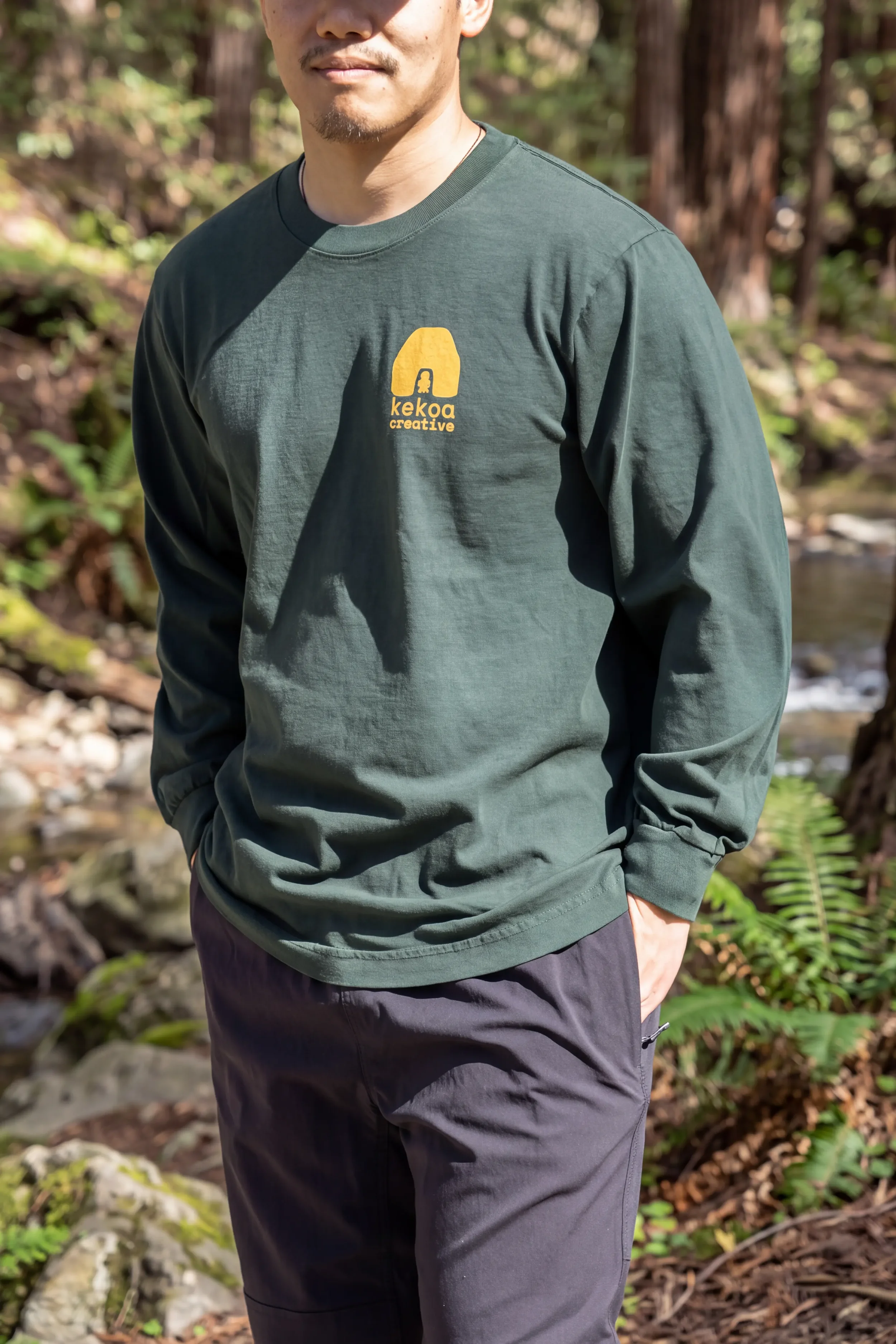 Model wearing unisex Nahele Green Kauila long sleeve reclaimed cotton trash tee with yellow chest logo by Kekoa Creative.