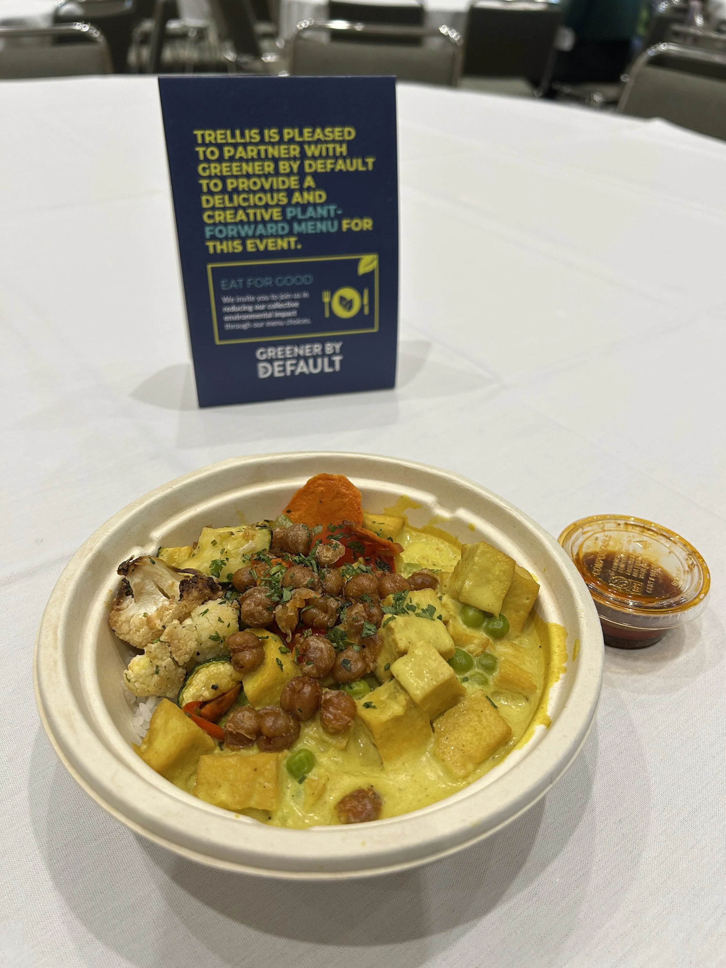 A chili crisp tofu bowl and table top sign from Greener by Default showcasing plant-based event menus
