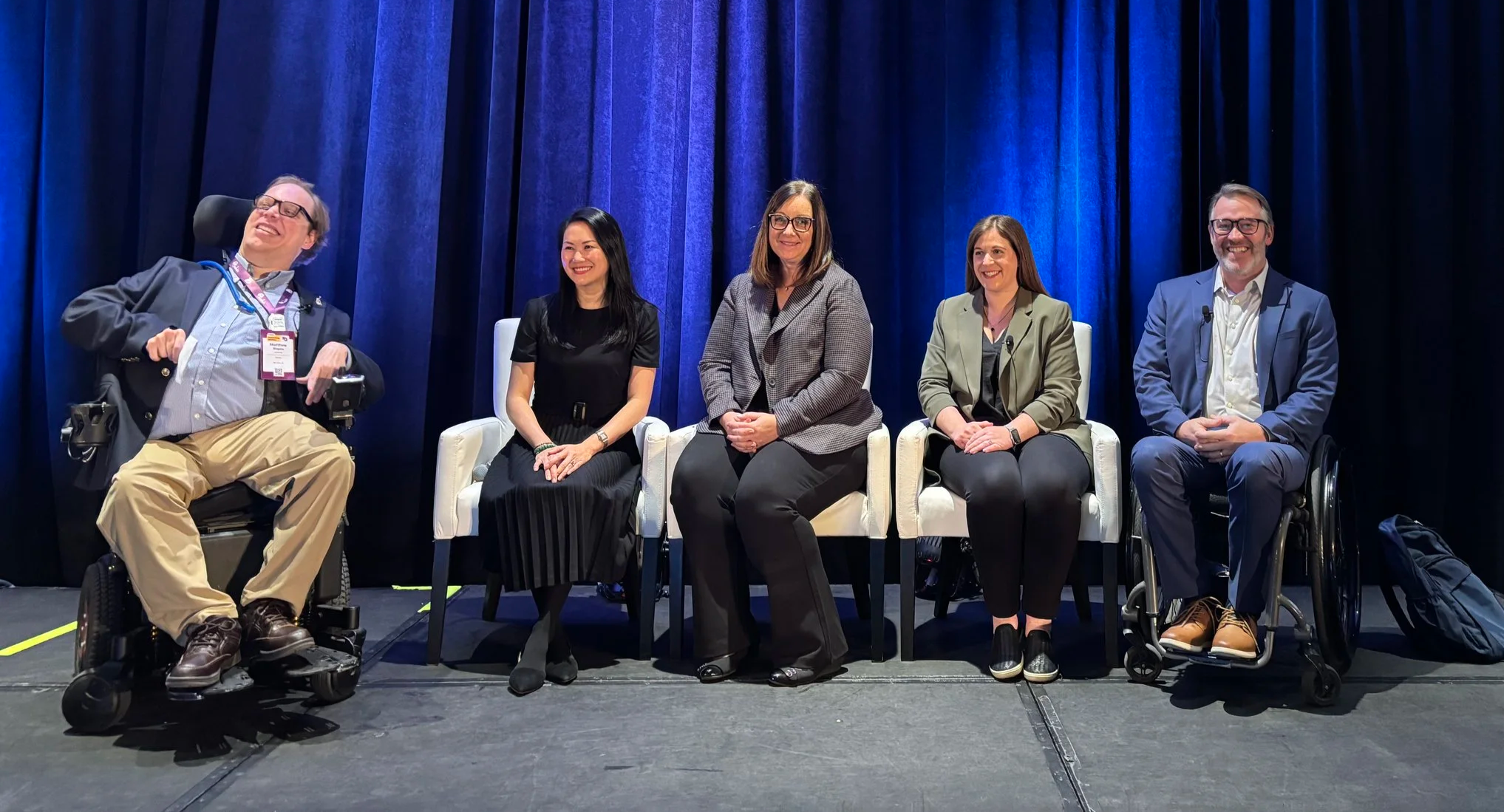An accessibility panel of five people at PCMA Convening Leaders 2026, showing two panelists in wheelchairs an three panelists in conventional chairs, seated on a stage in front of a blue curtain.