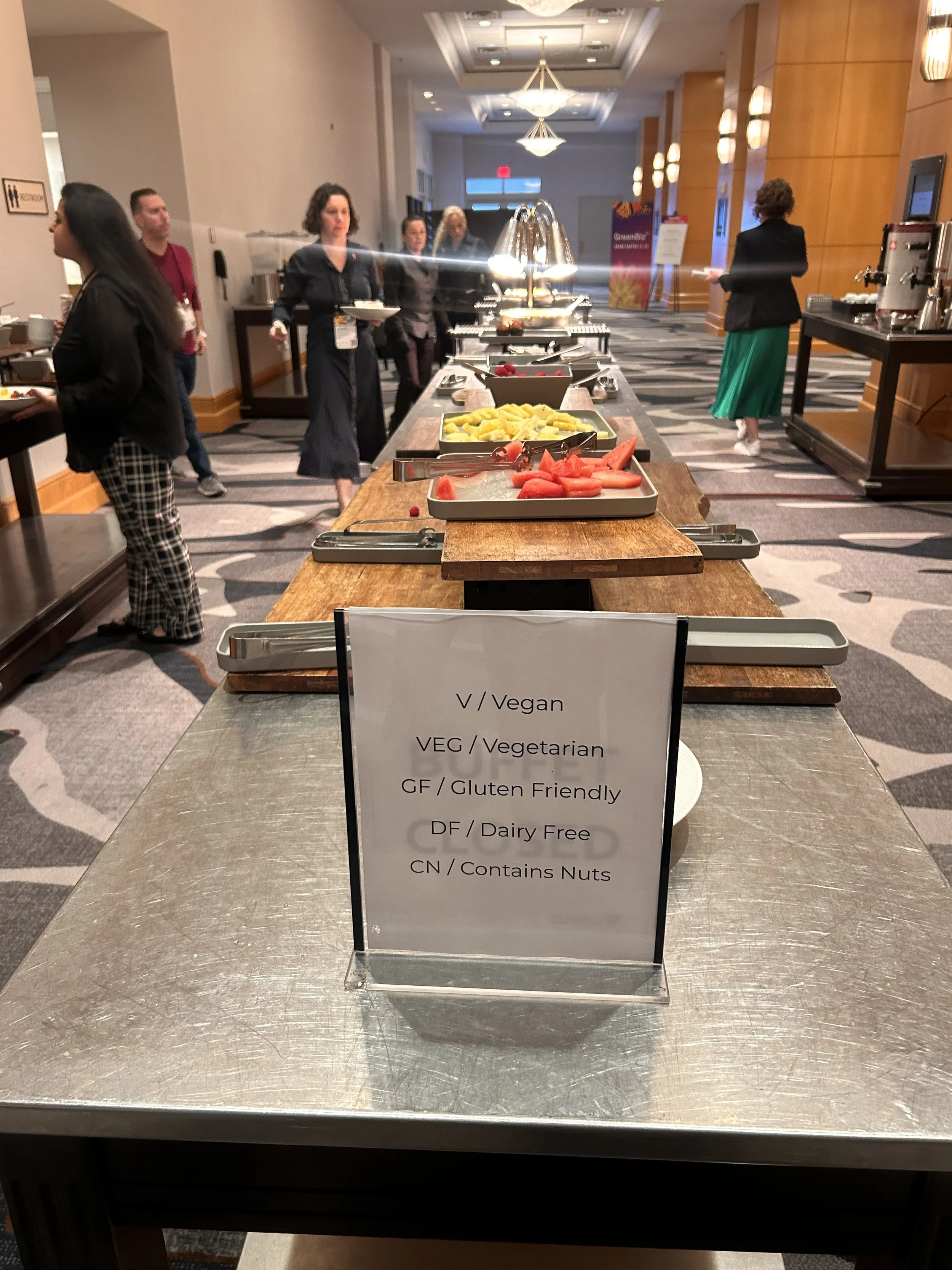 A buffet table with a sign containing a legend for food labeling for vegetarian, vegan, nut free, etc. items