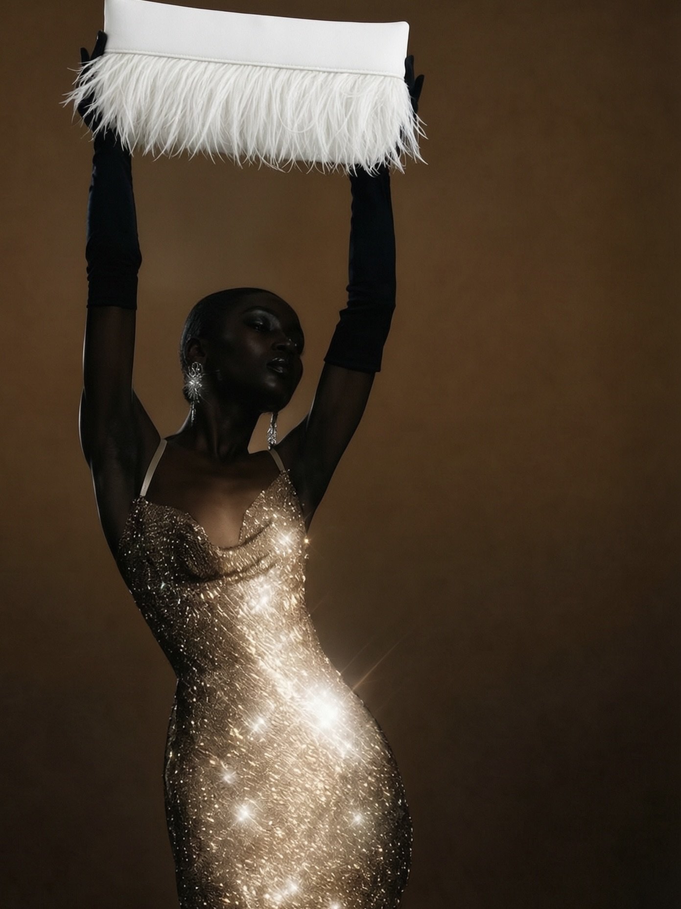A woman with dark skin and short hair wearing a gold, sparkly, fitted dress with spaghetti straps and black gloves, holding a white clutch with fringes above her head.