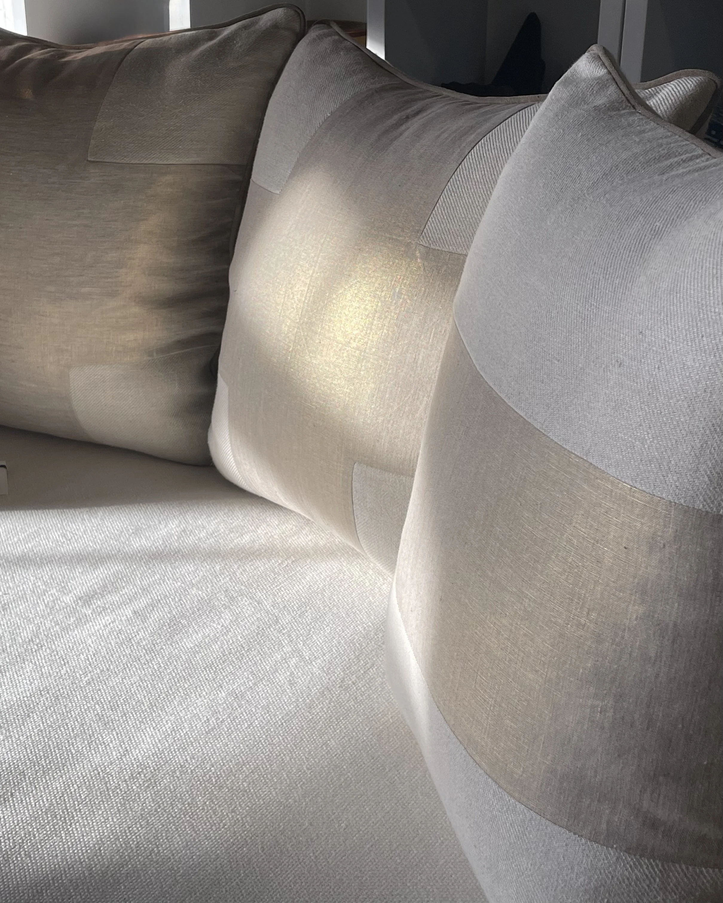 A close-up view of decorative throw pillows on a beige fabric sofa, showing different shades of beige and neutral tones.