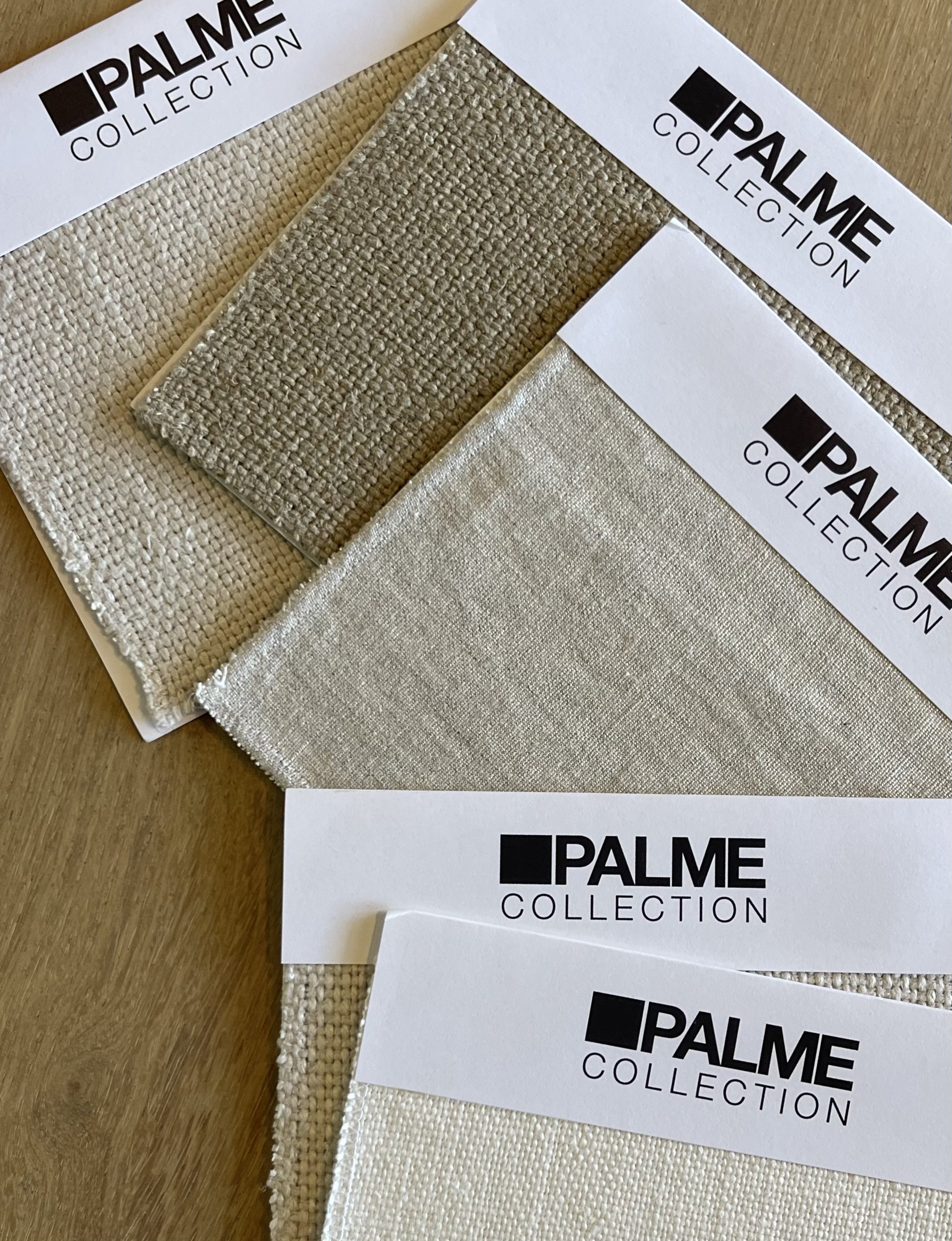 Three fabric swatches in different shades of beige and gray, each labeled with a white card reading 'PALME COLLECTION', arranged on a wooden surface.