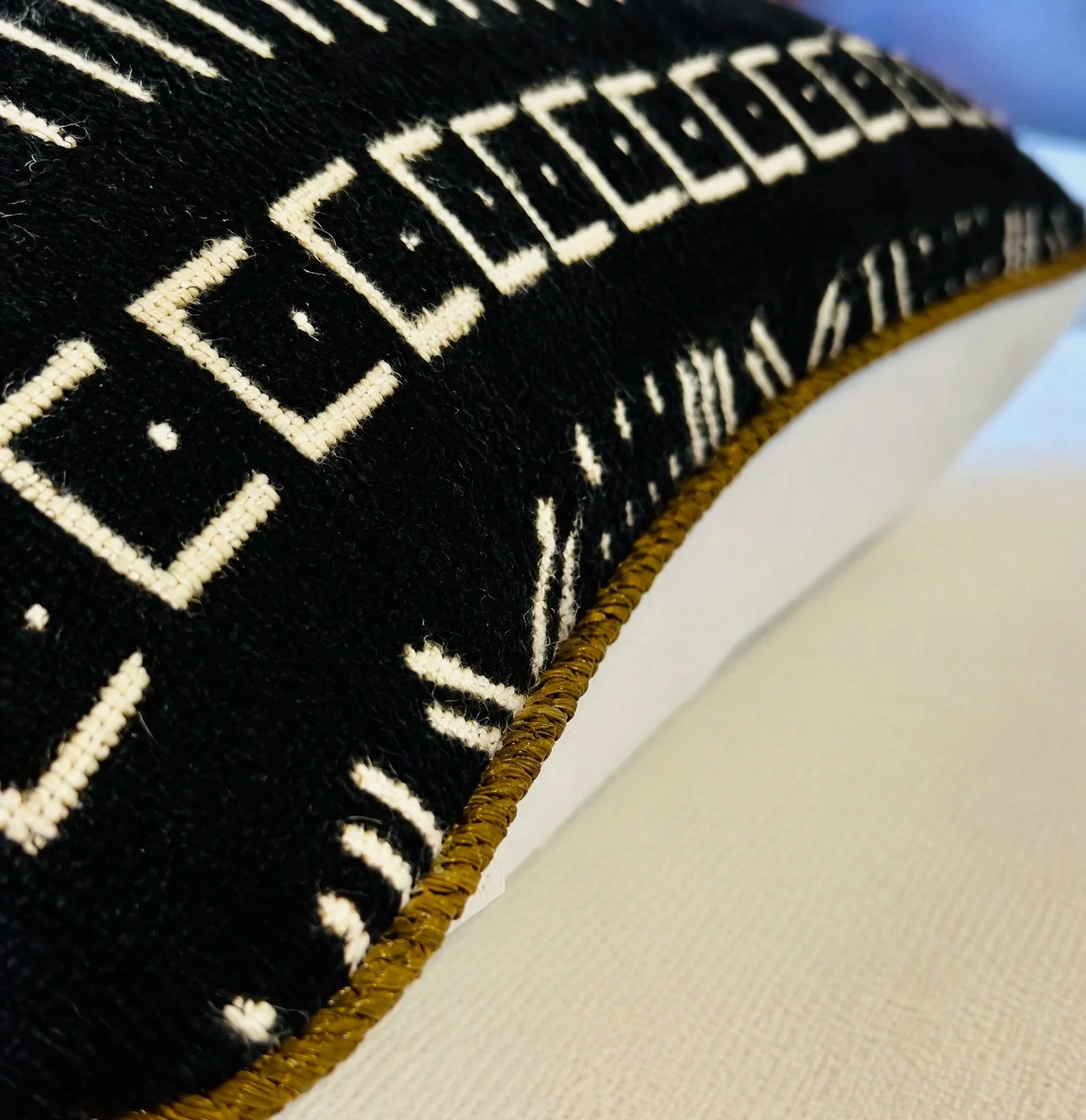 Close-up of a black embroidered fabric with white lettering on a gold woven border, placed on a white surface.