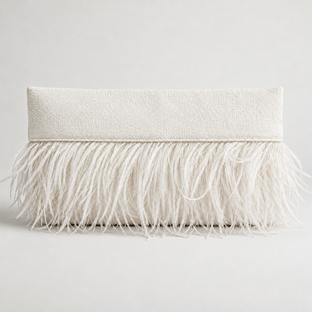 A white textured pillow with a feathered trim across the bottom, placed on a white surface against a plain white background.