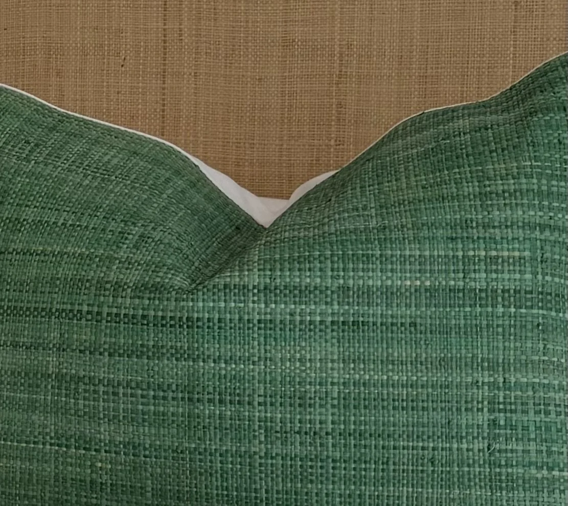 Close-up of a green woven fabric pillow on a beige textured surface.